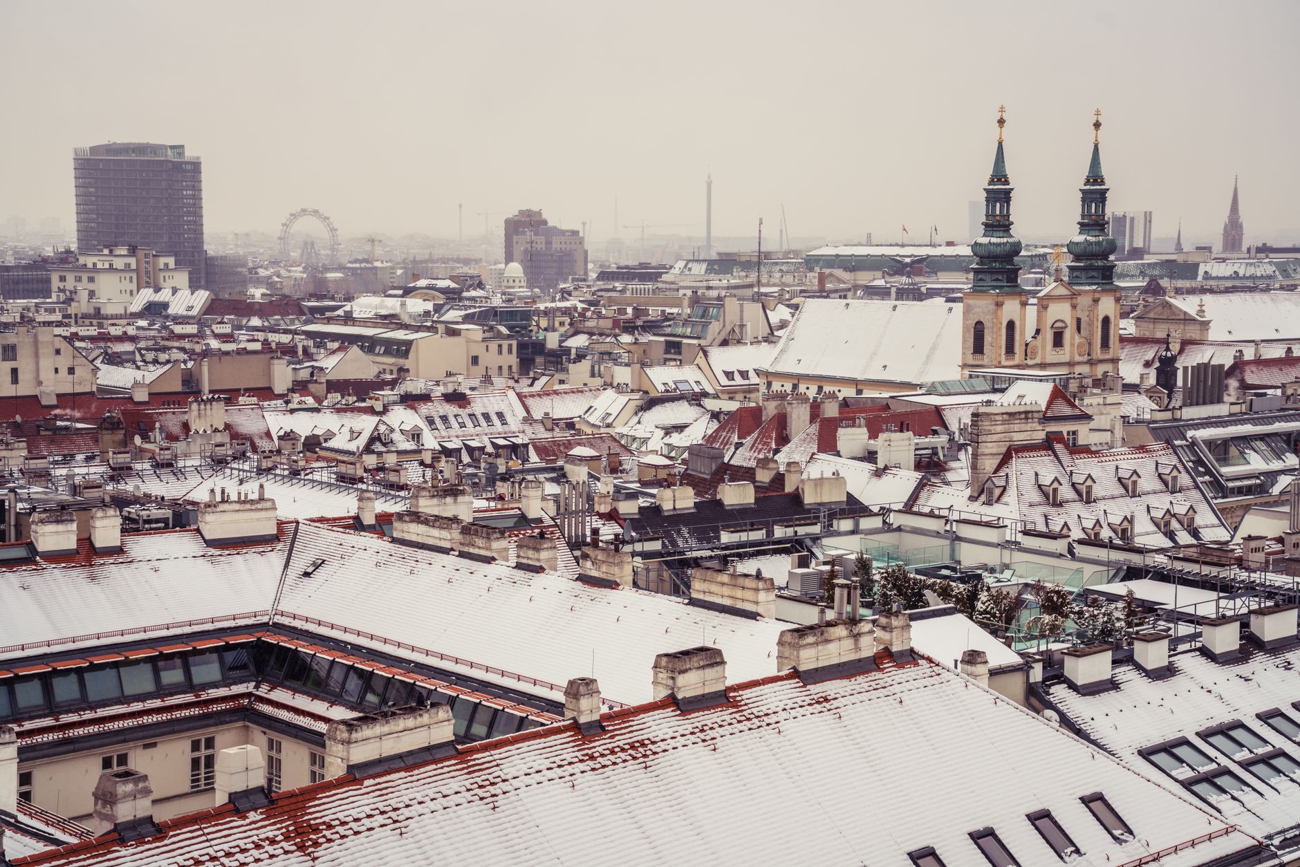 Sweeping view of Vienna's historic rooftops and church spires at sunset, with a mix of Baroque and modern architecture.