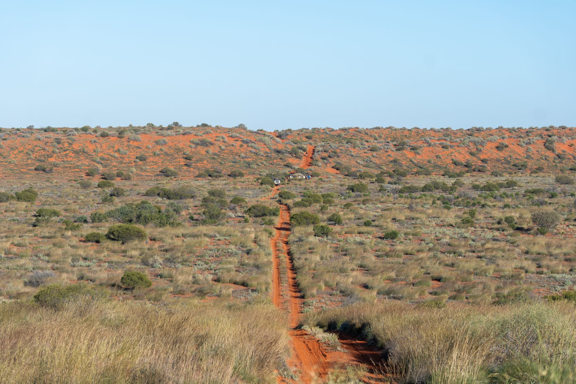 An aerial view of a winding coastal road meeting a vast, rugged Australian landscape under a dramatic sunrise, hinting at a long journey.