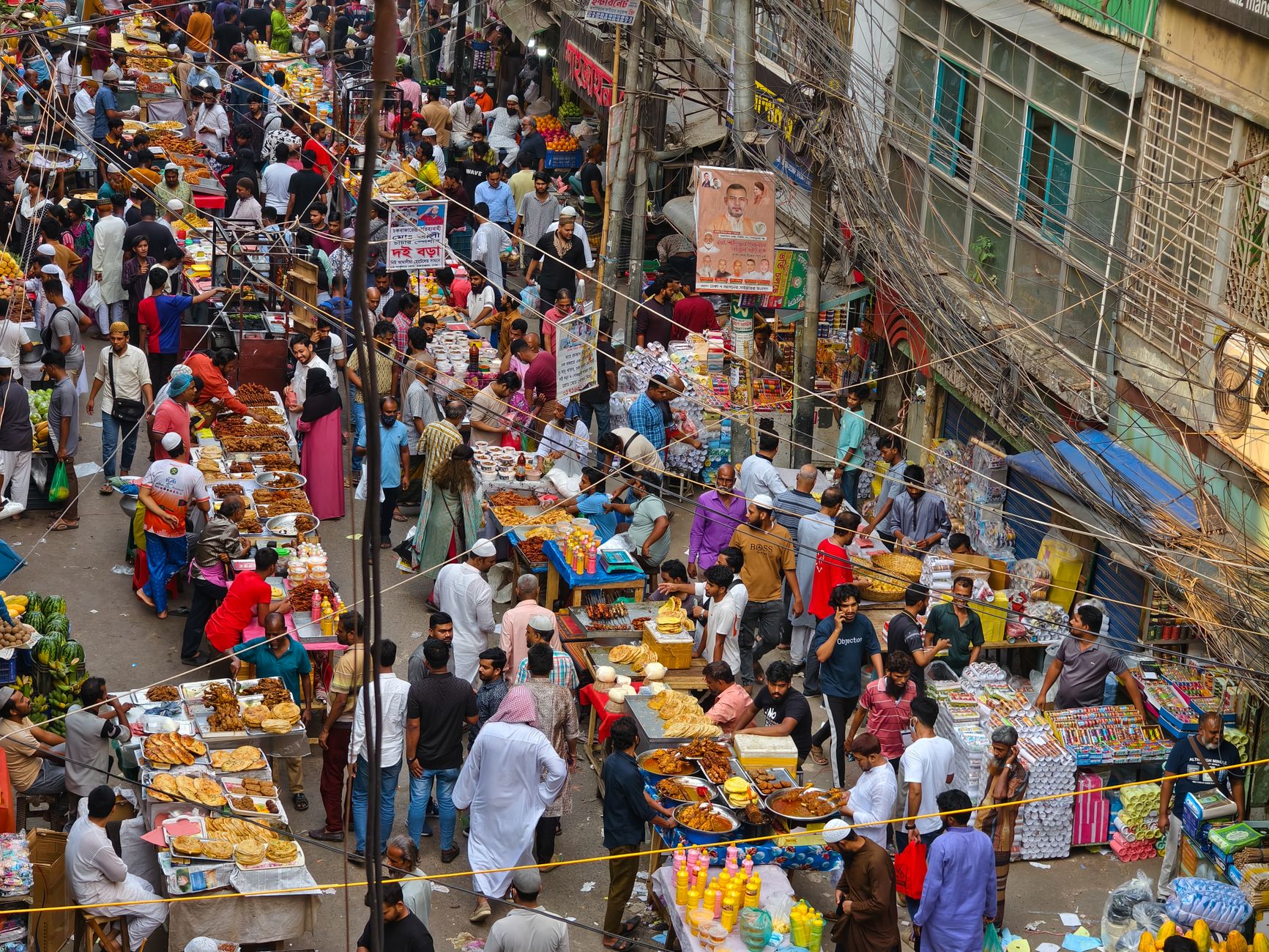 A bustling, vibrant street food market in Lahore's old city at dusk, with food stalls glowing under string lights and crowds of people enjoying meals.