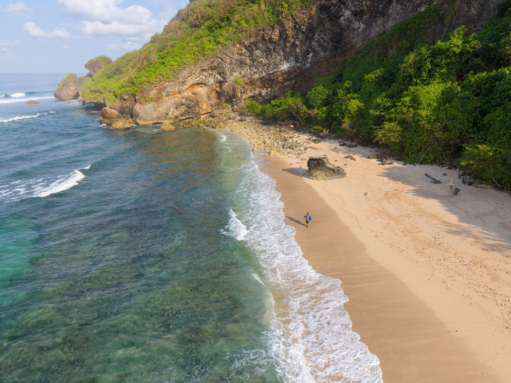 A sweeping aerial view of an untouched white sand beach meeting clear turquoise waters on a remote Asian island, with lush green jungle bordering the sand and no visible human activity.
