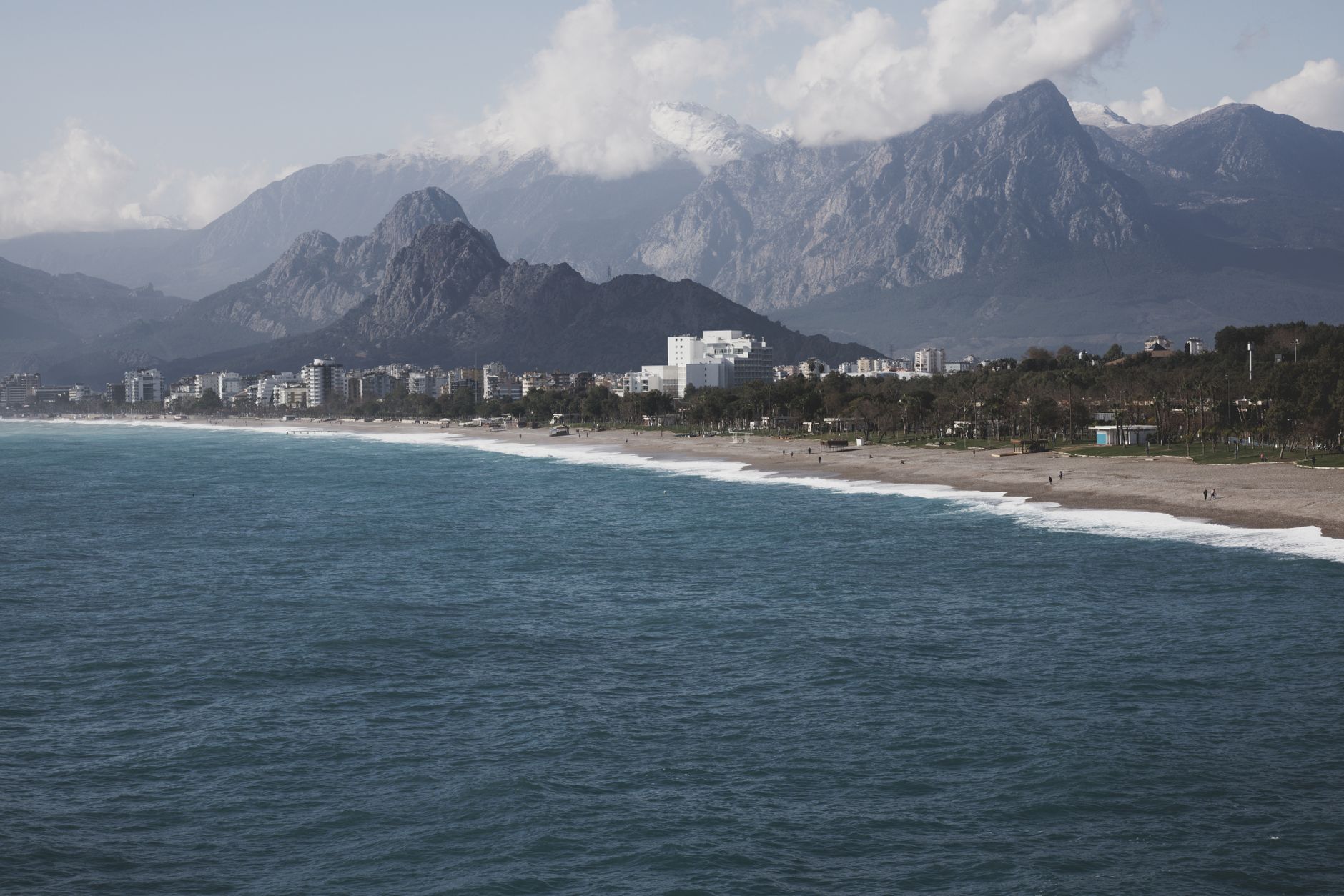 A split image showing a serene, untouched beach with turquoise waters on one side and majestic, rugged mountains under a clear sky on the other, symbolizing a choice between two distinct travel experiences.