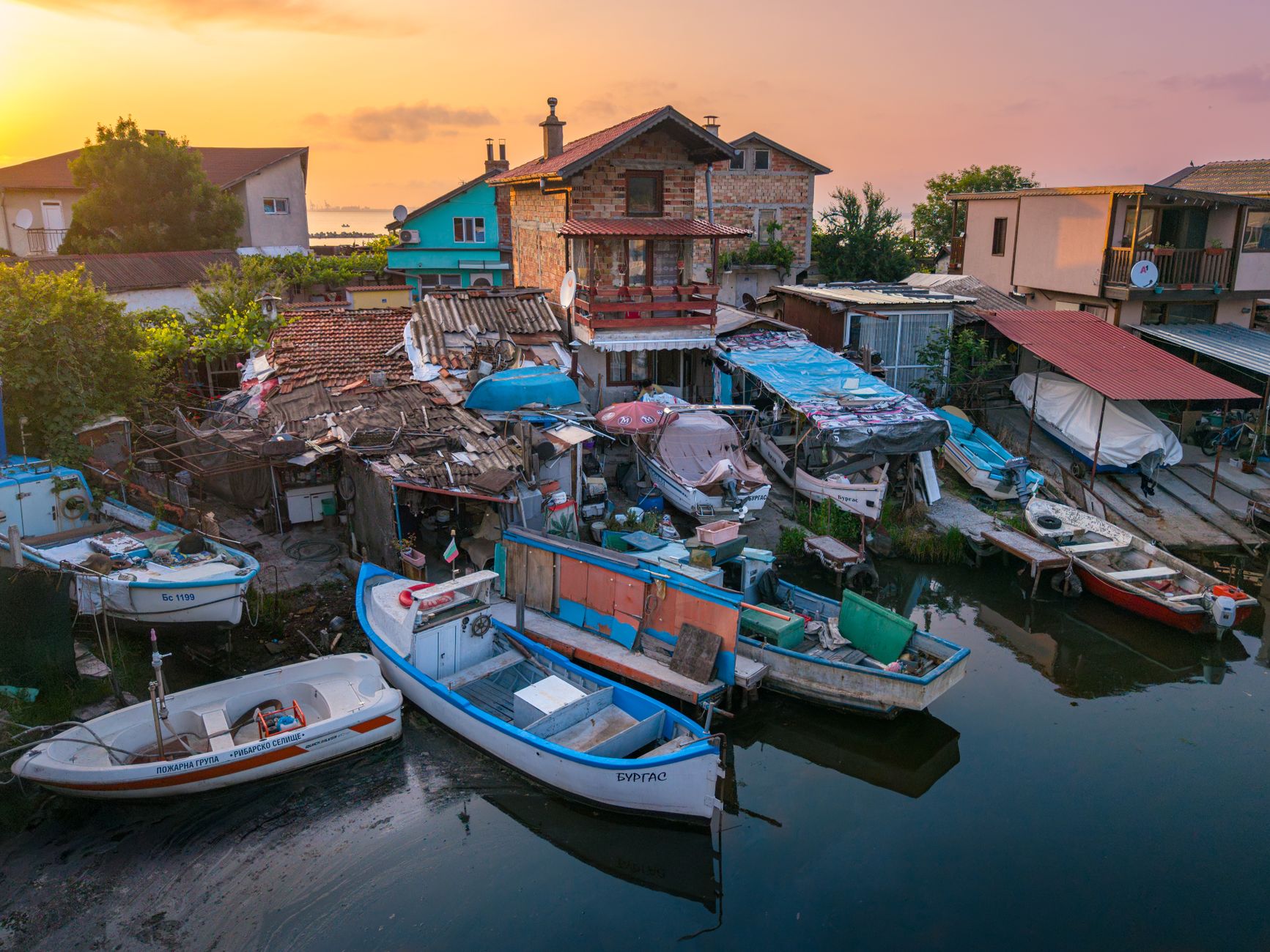 Sweeping view of a remote fishing village at dawn, with traditional boats silhouetted against the rising sun.