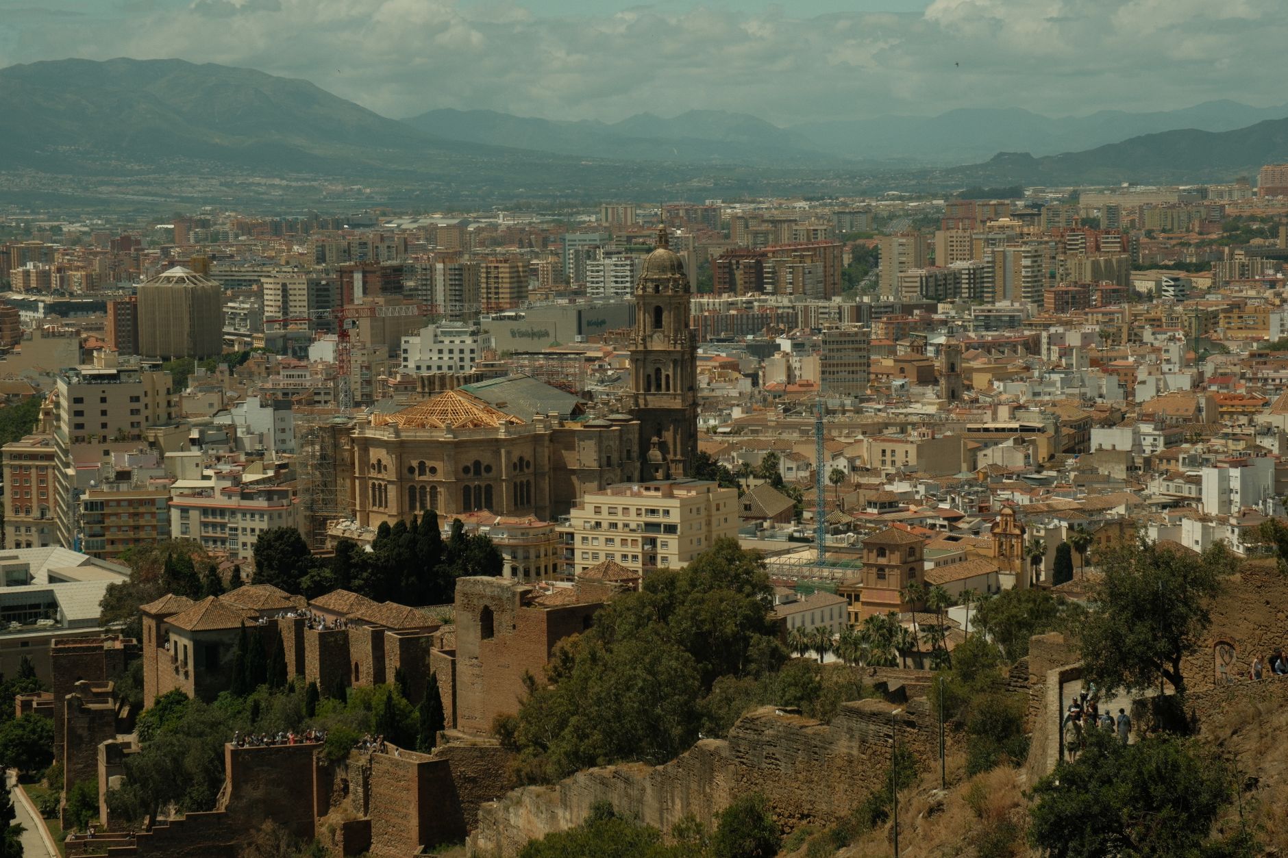 An aerial view of an ancient city built into a cliffside, revealing distinct historical layers of architecture and geological strata.