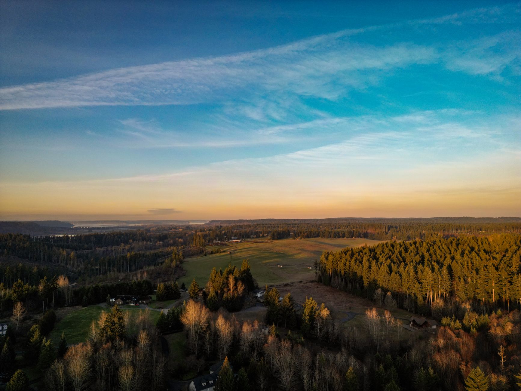 A sweeping aerial view of a dramatic, rugged Washington State landscape featuring evergreen forests, a winding river, and distant mountains under a cloudy sky.