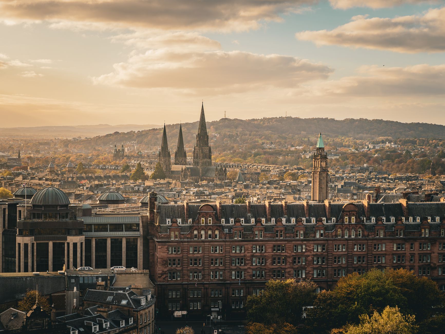 Sweeping panoramic view of Edinburgh's historic Old Town, with Edinburgh Castle prominent on Castle Rock and the Royal Mile winding down towards Holyrood Palace, under a dramatic sky.
