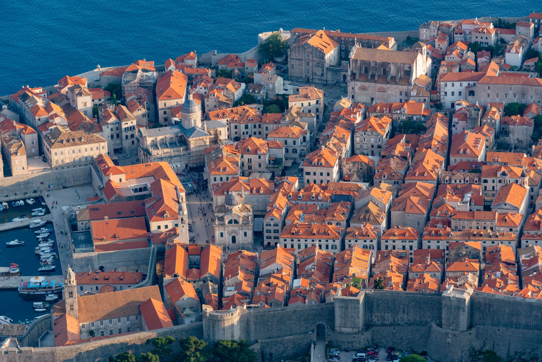 An aerial view sweeping over a ancient, fortified European town, showing rooftops, narrow streets, and surrounding green landscapes, hinting at hidden stories.