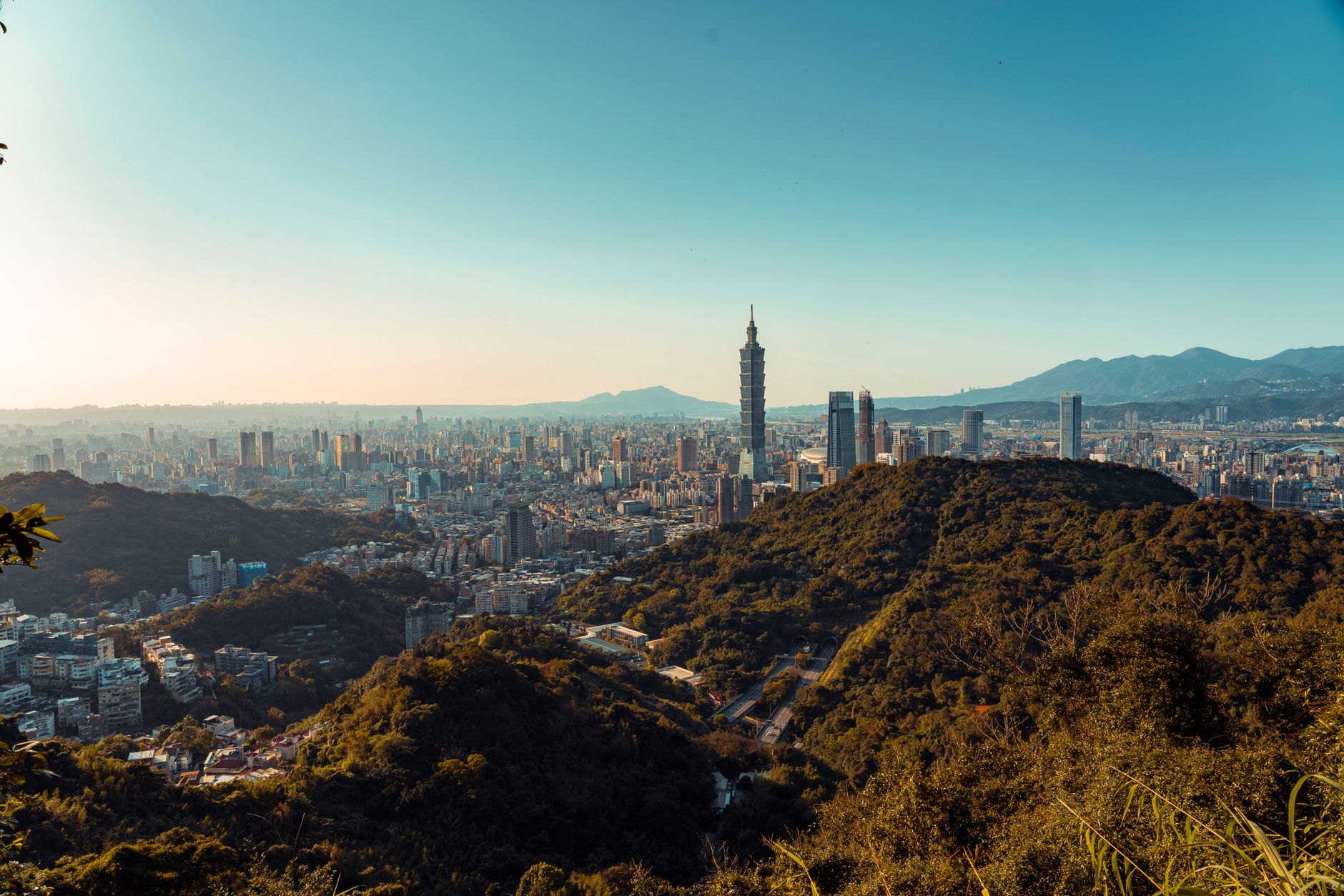 Sweeping aerial view of a dramatic mountain range meeting an ancient European city skyline at dawn, with mist clinging to peaks and historic buildings.