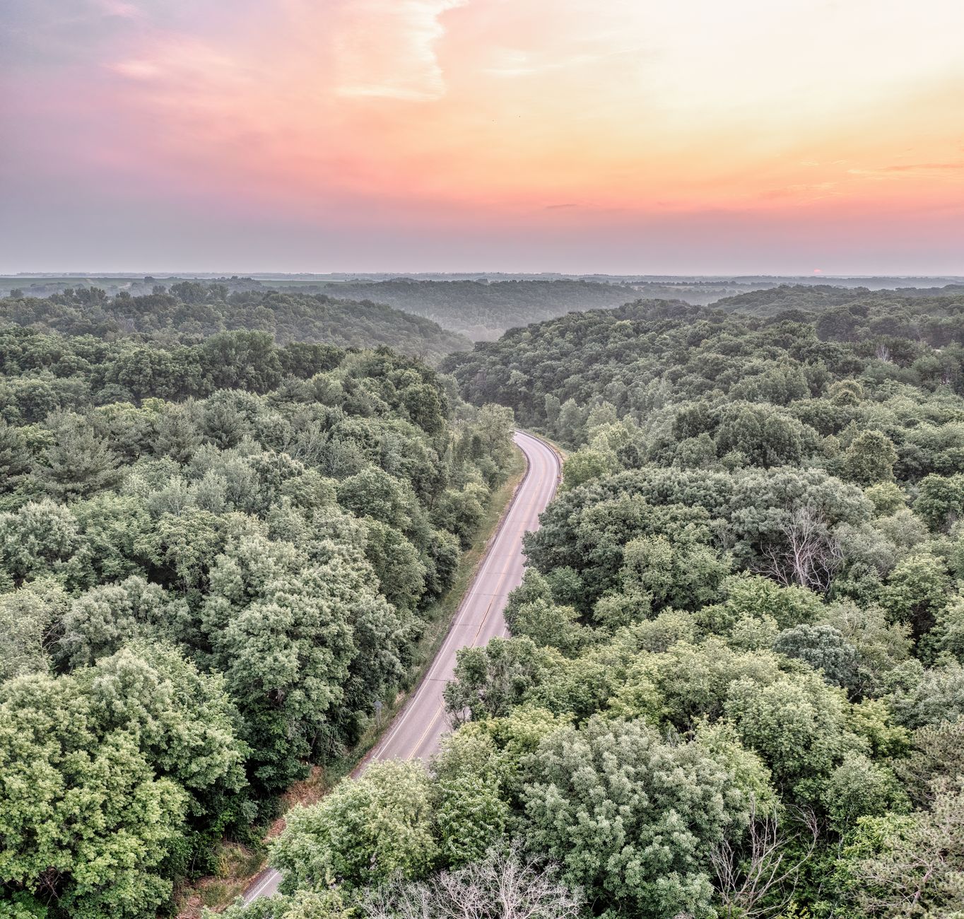 A winding road stretching through a vibrant autumnal landscape, leading towards a small, picturesque town under a colorful sunset sky.