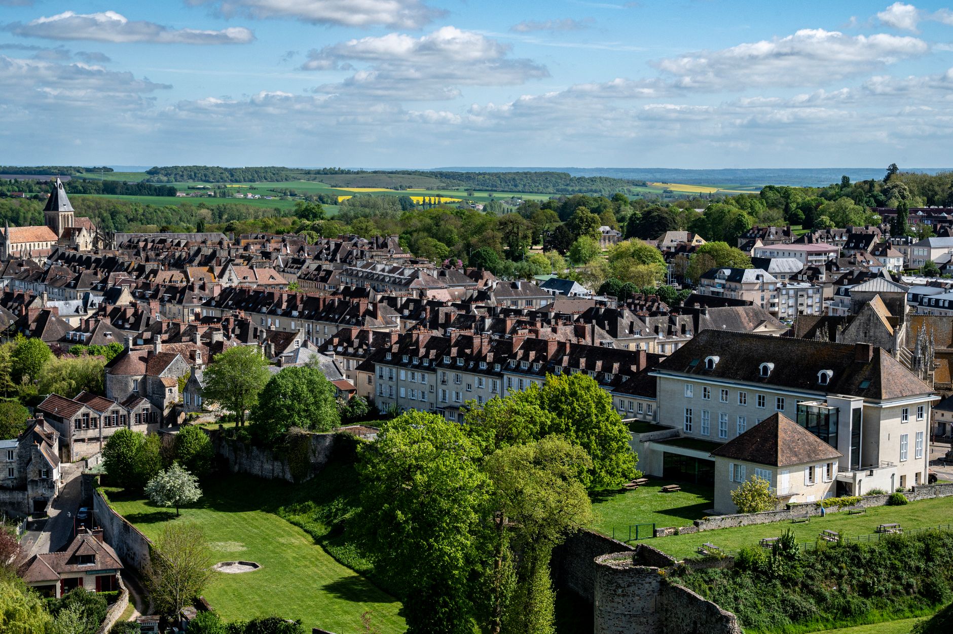Sweeping panoramic view of a picturesque medieval French village nestled in a verdant valley, with historic stone buildings and a winding river.