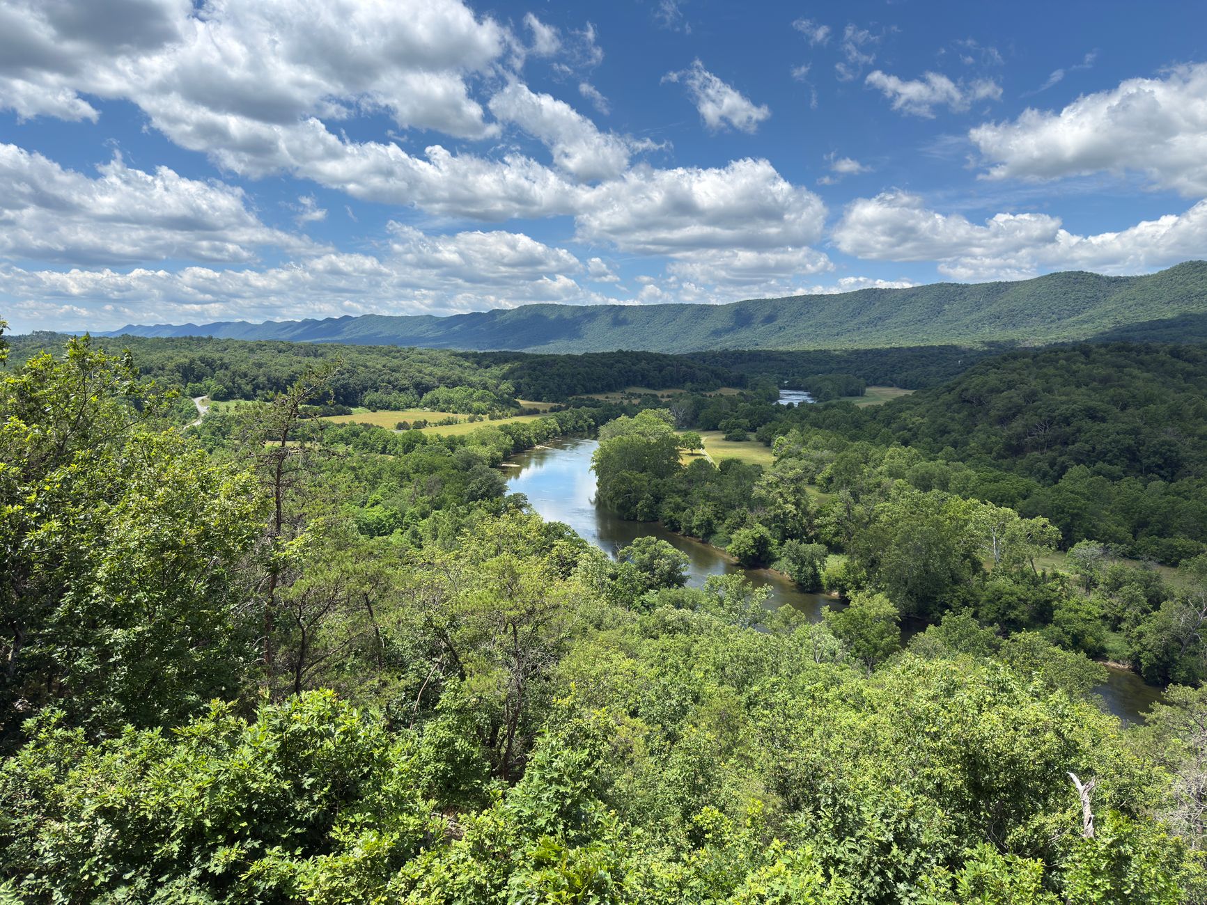 Sweeping aerial view of the Virginia Creeper Trail winding through a lush, forested Appalachian valley with a river beside it.