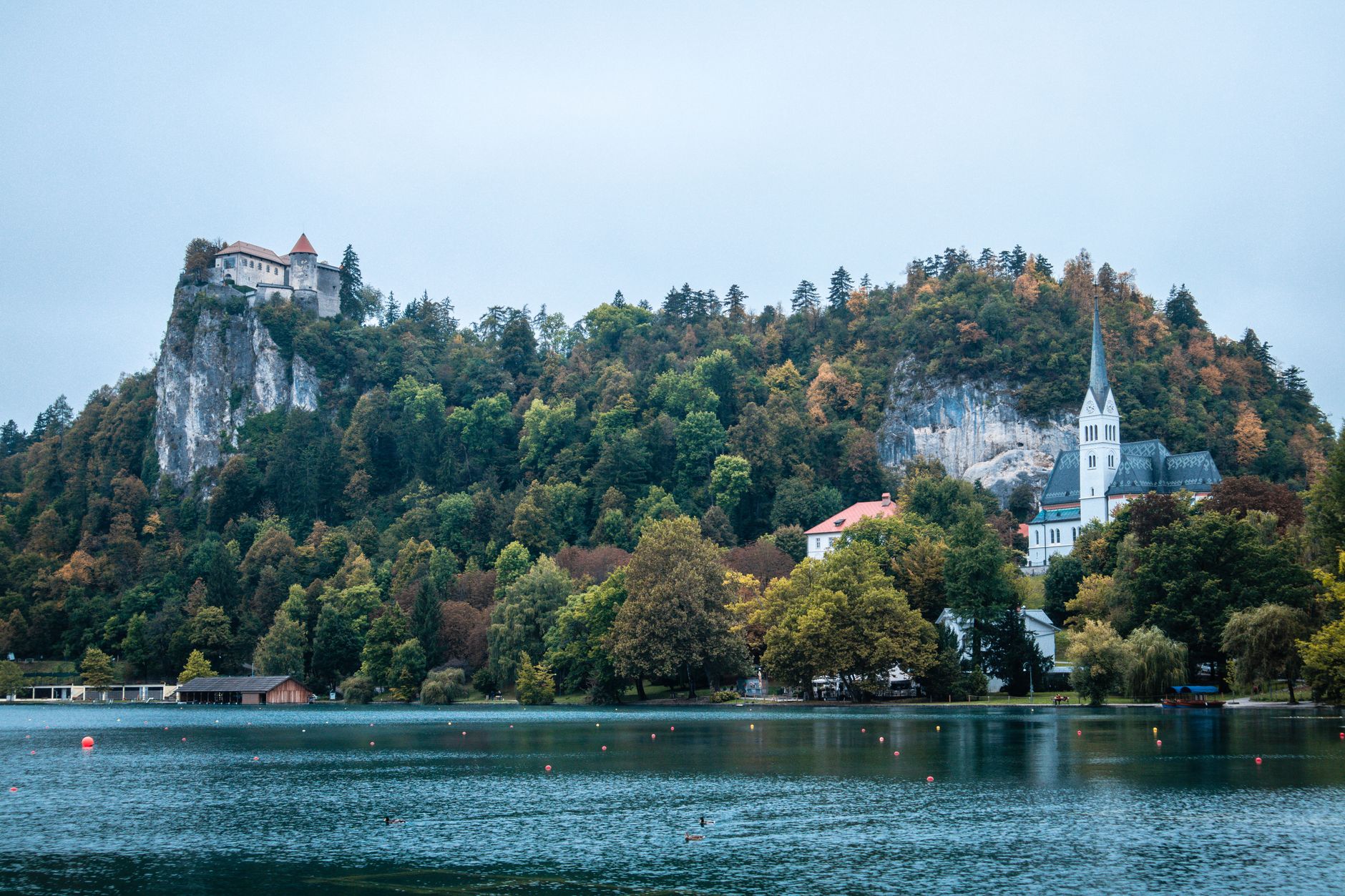 Panoramic view of a medieval Slovenian town with red roofs against a backdrop of rolling green hills and distant mountains under a clear sky.