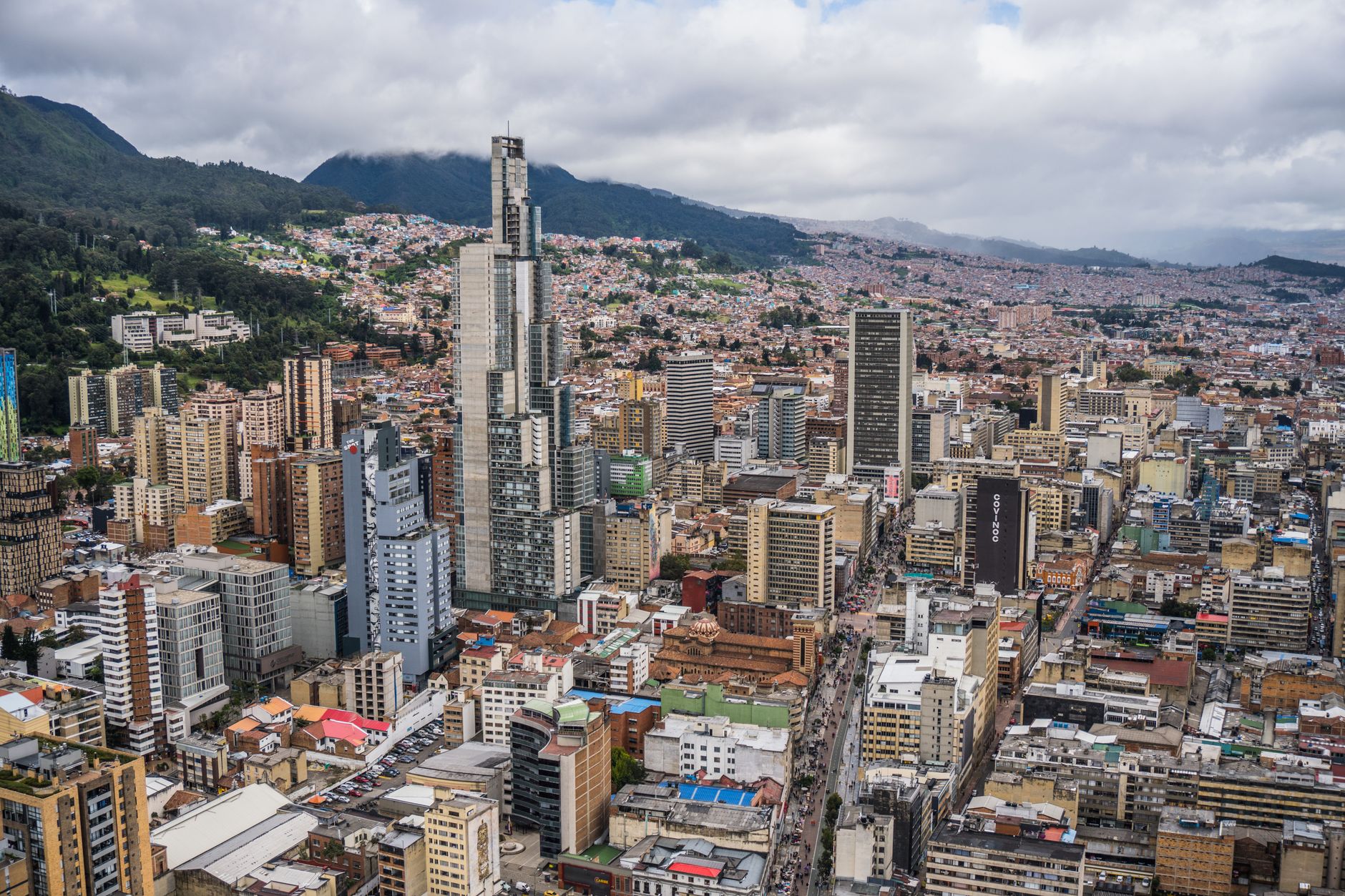 An aerial view of Colombia's diverse landscapes, showing lush green mountains, a winding river, and distant arid plains under a bright sky, symbolizing the country's varied natural beauty.