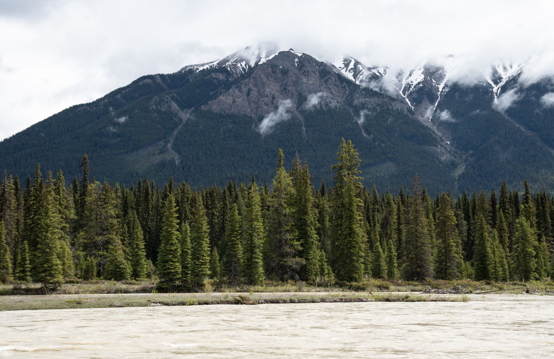 Sweeping view of a vast, untouched Canadian wilderness with mountains, forests, and a clear lake under a blue sky, conveying a sense of adventure.
