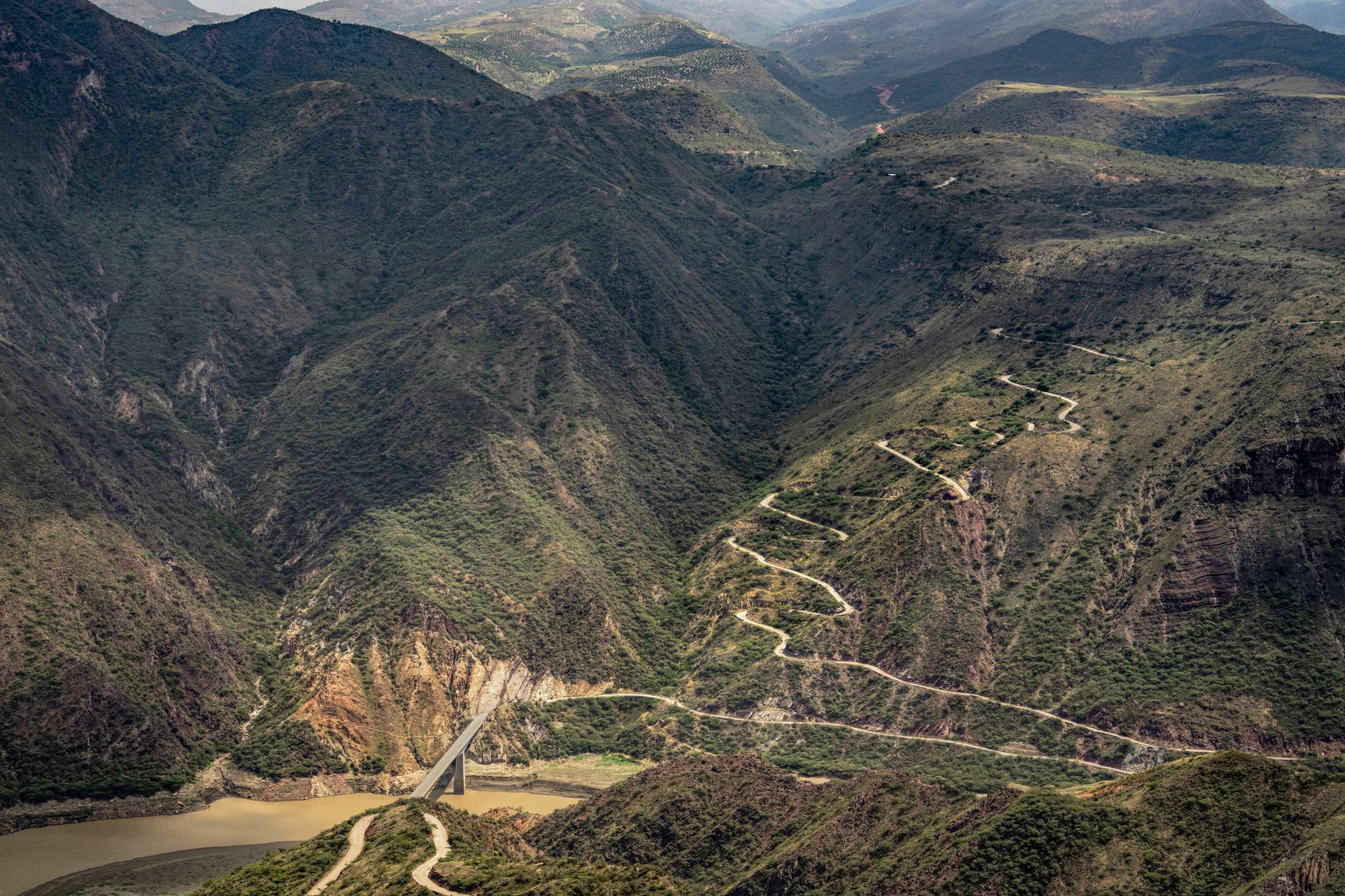 An aerial view of a winding road cutting through a vast, dramatic mountain landscape under a clear sky, evoking a sense of adventure.
