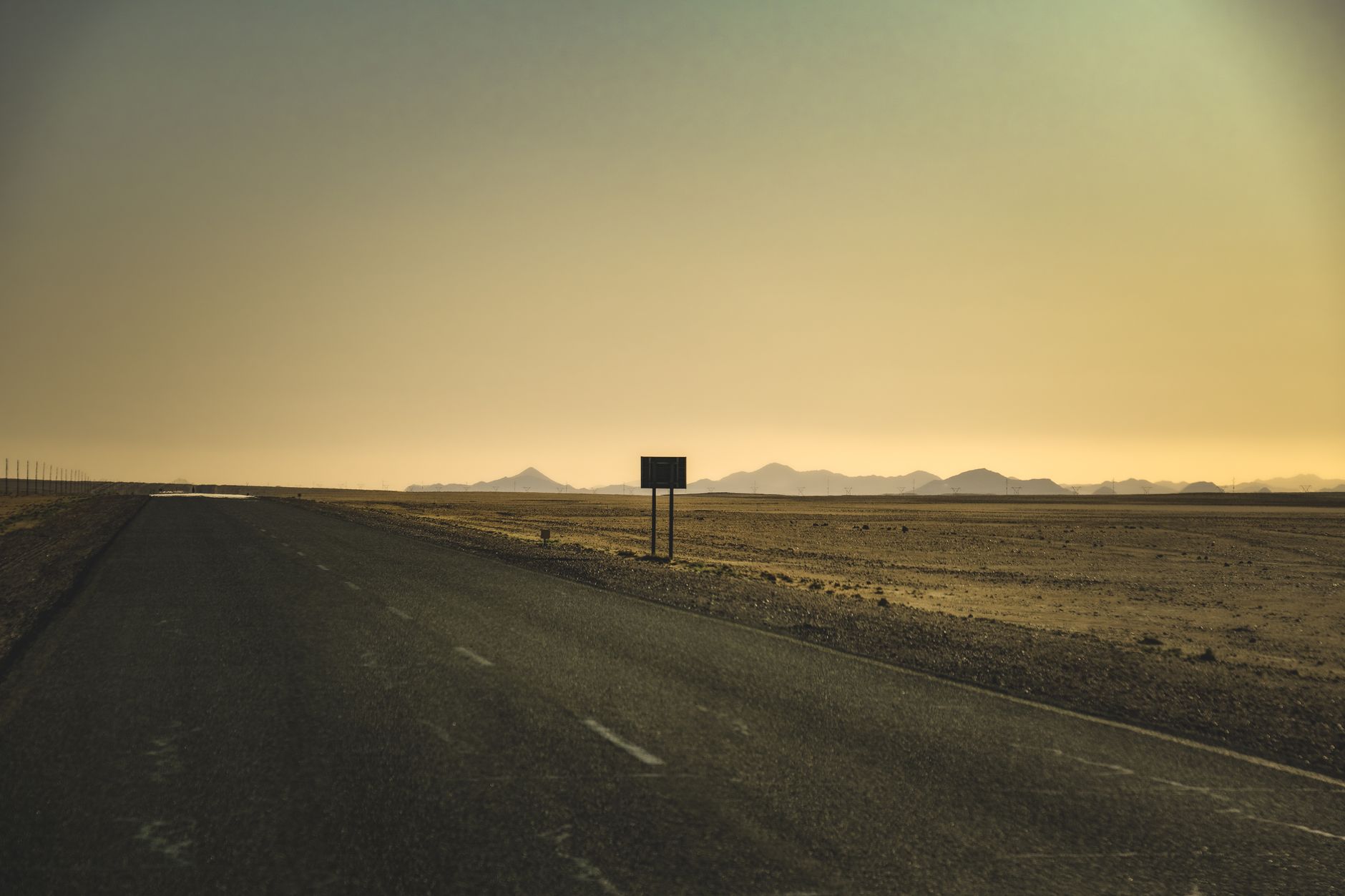 A winding road stretches into the distance through a vast, dramatic desert landscape under a colorful sunset sky, inviting long-distance travel.