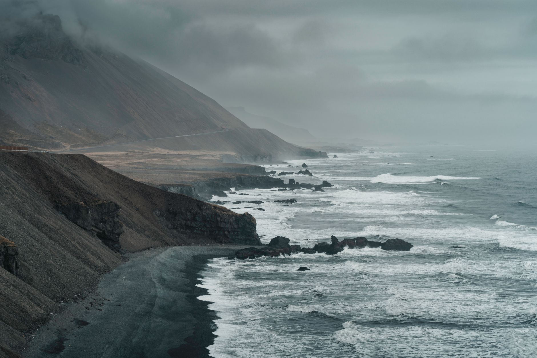 Sweeping view of a rugged, cool coastline with fog rolling in, suggesting varied temperatures and atmospheric conditions.
