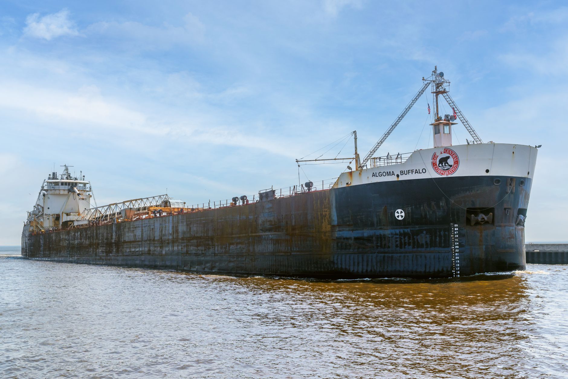 An aerial view of a cargo ship navigating a wide, calm stretch of the St. Lawrence Seaway, flanked by lush green landscapes.