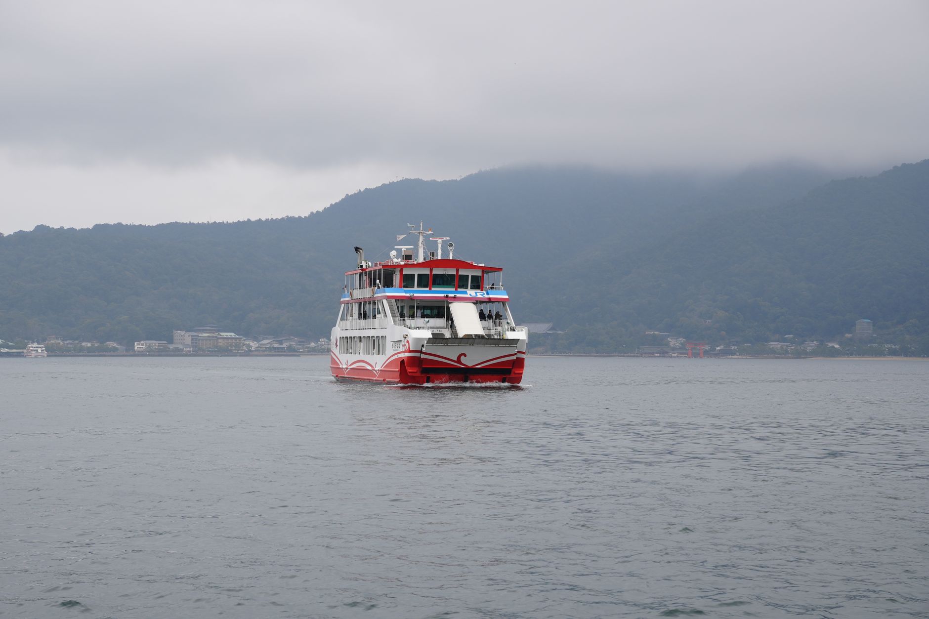 Sweeping panoramic view of Miyajima island showing lush green mountains, traditional buildings, and a glimpse of the Seto Inland Sea.