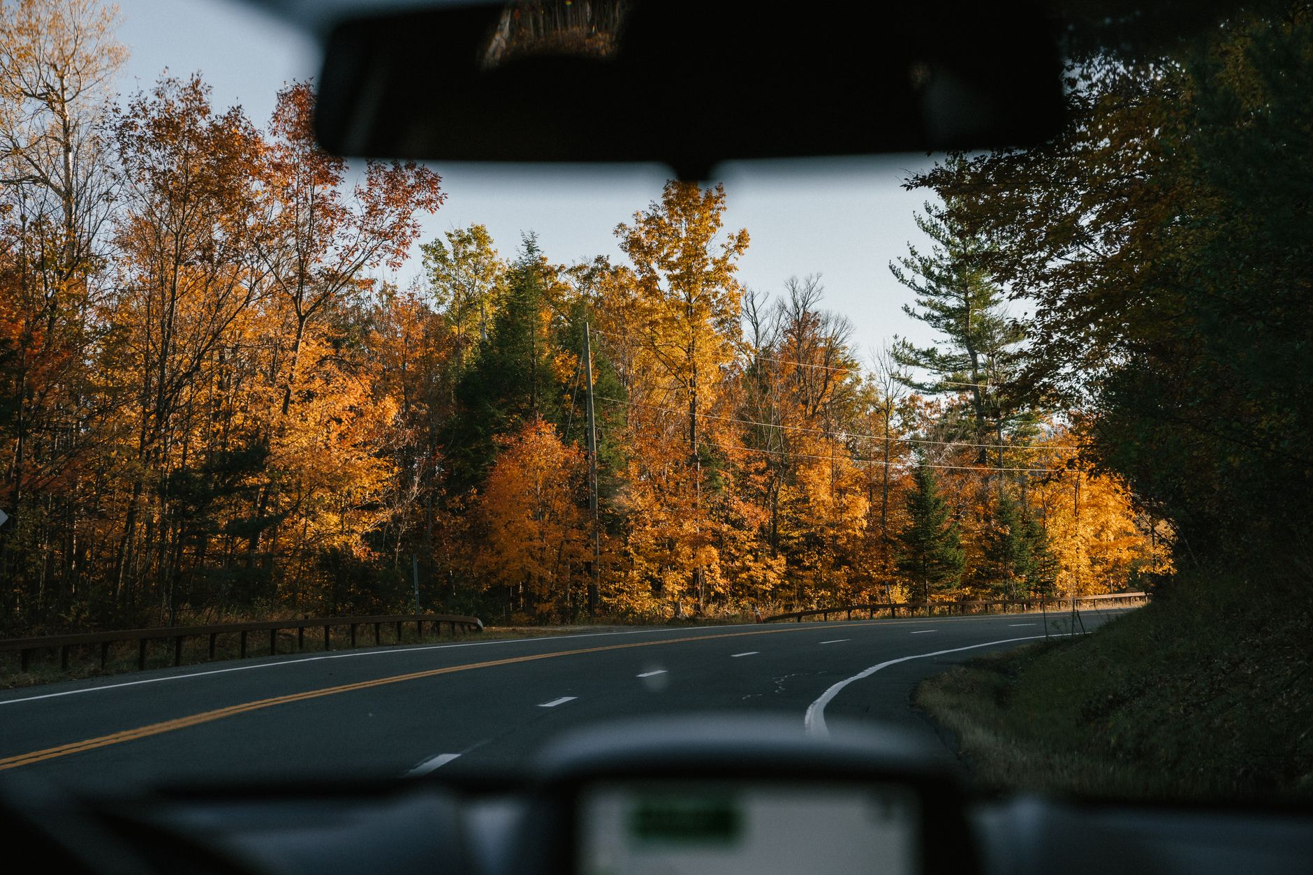 A winding road through vibrant autumn foliage in the Canadian countryside, with a glimpse of a large river in the distance, evoking a long, scenic journey.