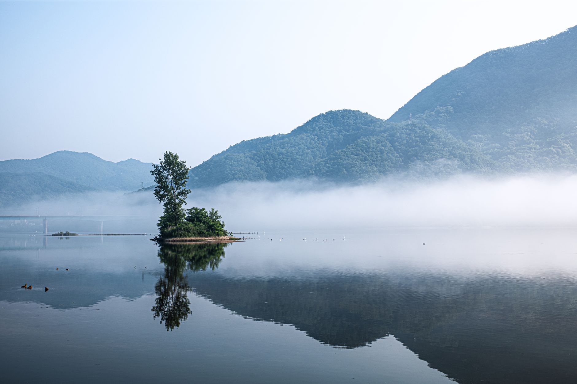 A serene traditional Korean pavilion with a tiled roof, nestled in a lush green mountain landscape under a clear sky.