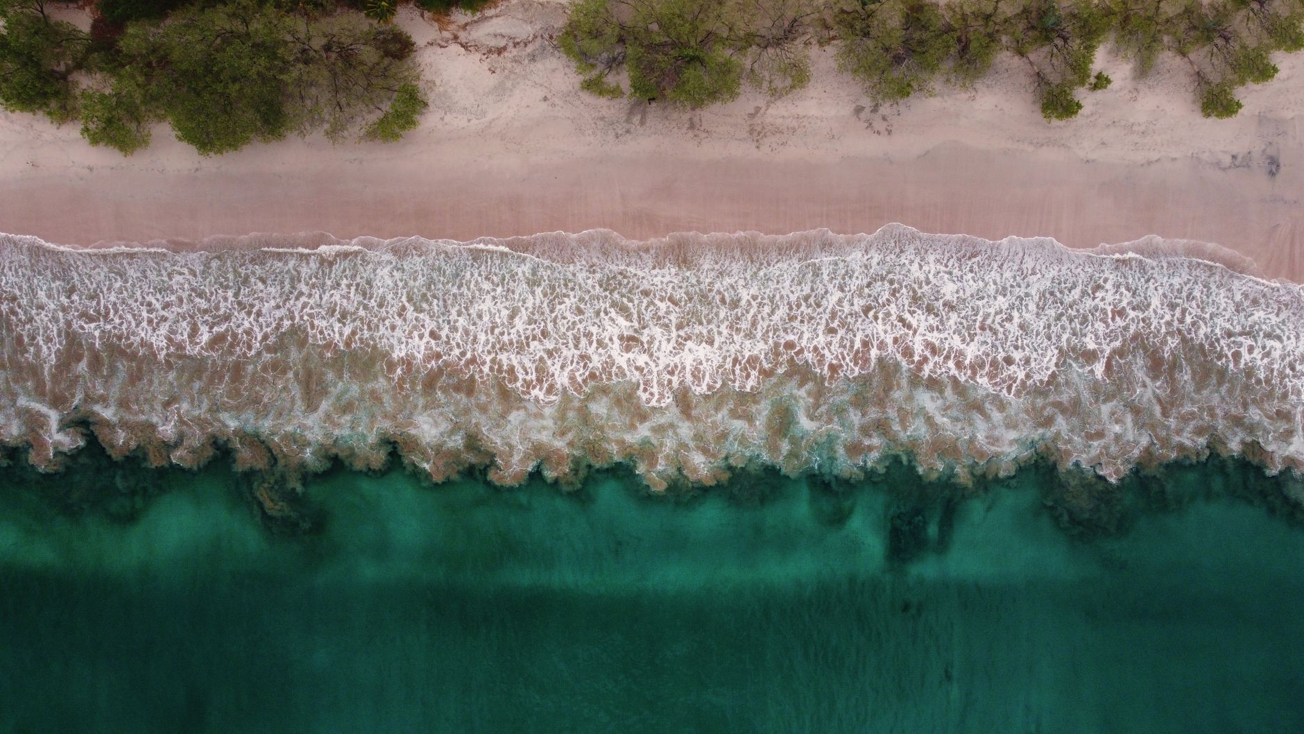 Aerial view of a pristine, wild beach in Guanacaste, Costa Rica, with lush green jungle meeting the turquoise ocean and rugged rock formations.