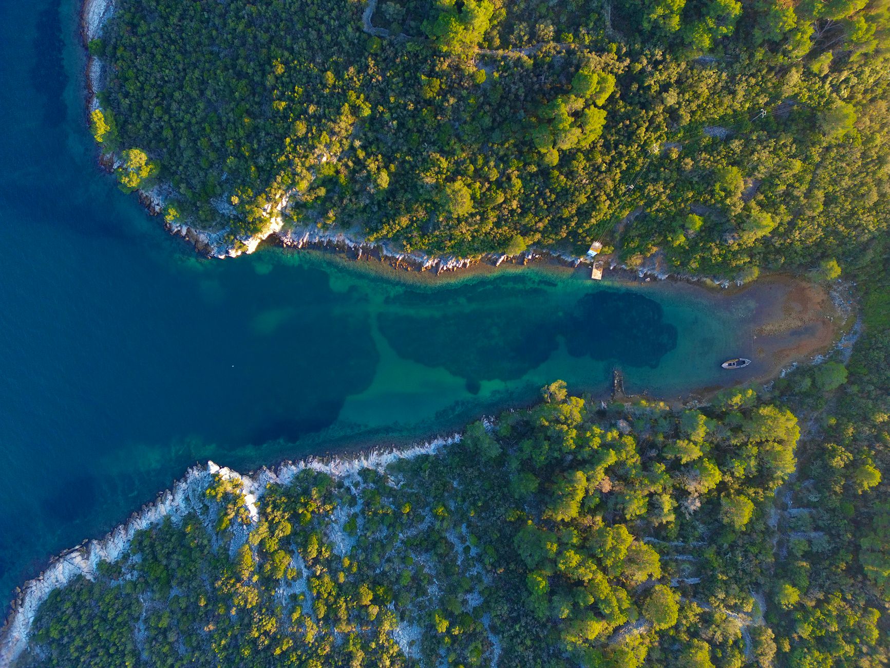 An aerial view of a secluded, pristine hidden cove on the Croatian coast, with turquoise waters and lush green cliffs, inviting exploration.