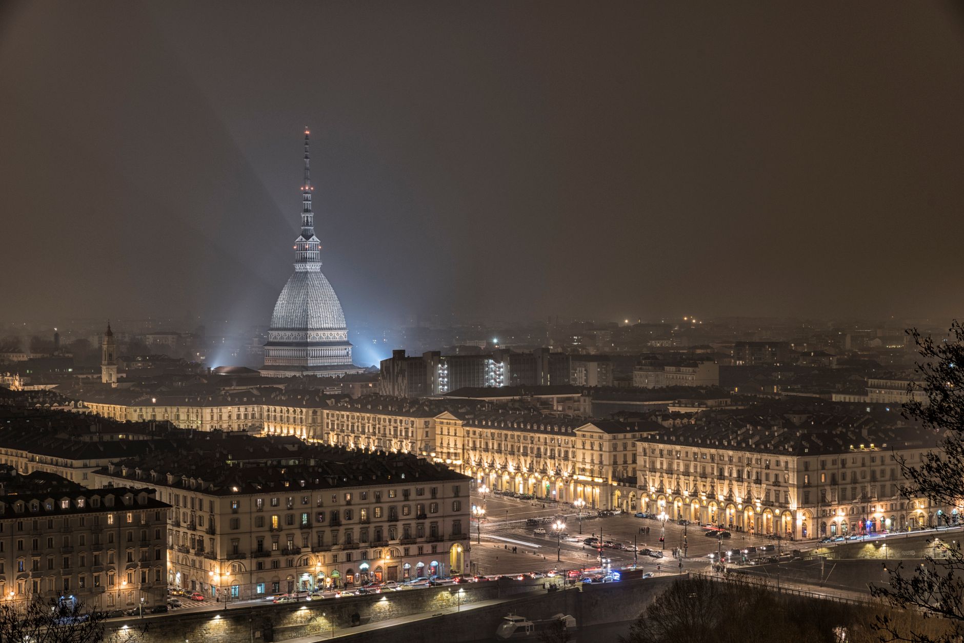 A panoramic view of Turin's historic center, showcasing a mix of Baroque architecture, narrow cobblestone streets, and the distant Alps under a clear sky.