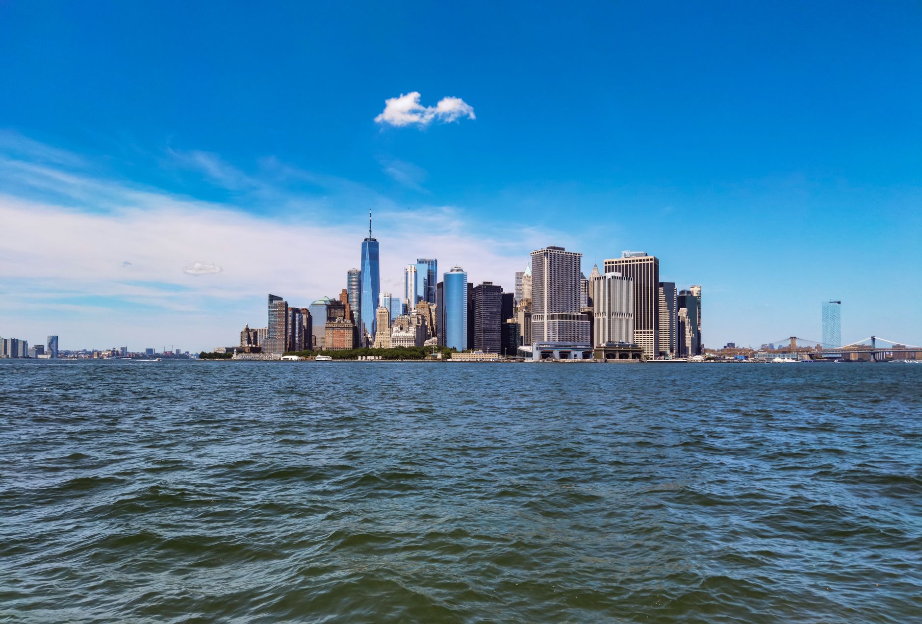 Panoramic view of a bustling New York City park hosting a summer concert, with diverse crowds enjoying music and food stalls under a clear sky.