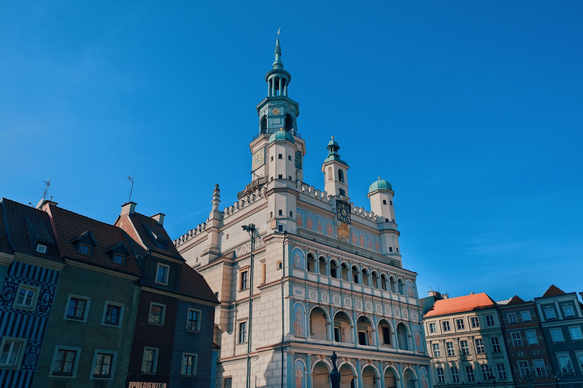 A sweeping panoramic view of Poznan, Poland, showing a blend of historic architecture and modern urban landscape under a warm sunset sky.