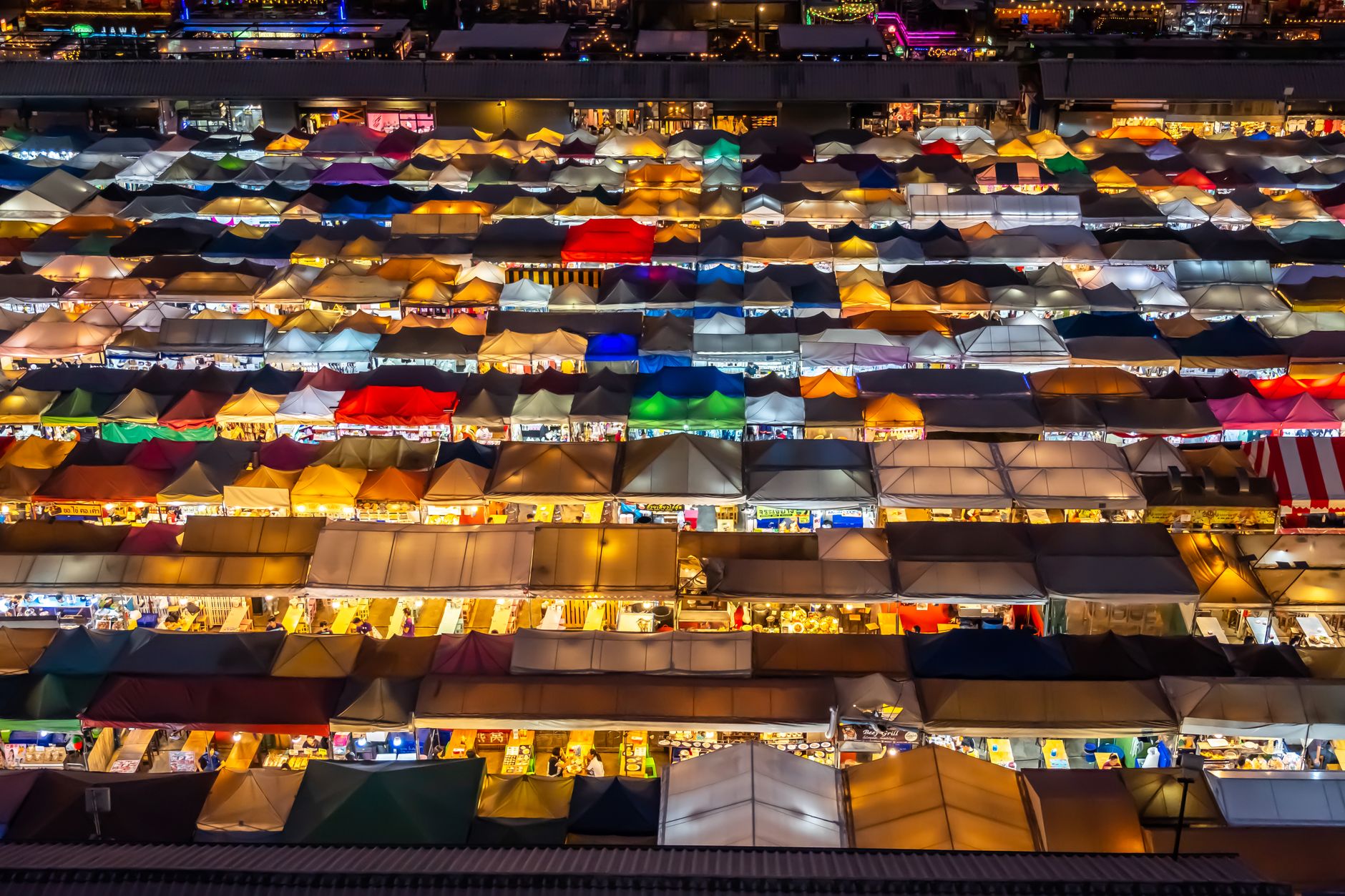A vibrant aerial view of a bustling street food market at night, with various stalls illuminated and people enjoying meals, showcasing the energy of Southeast Asian culinary scenes.
