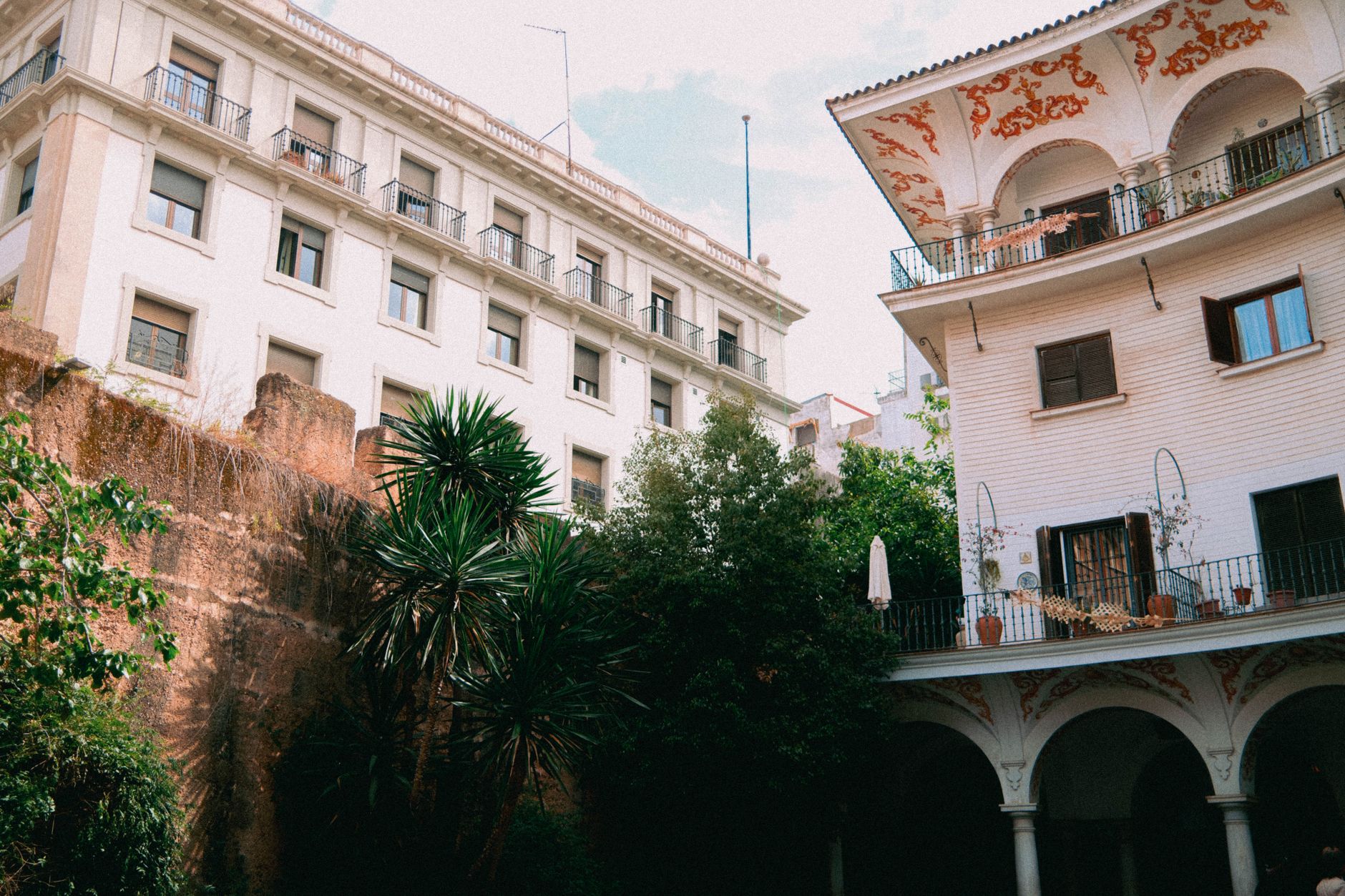 Sunlight filtering into a quiet, plant-filled courtyard in Seville, revealing ornate tiles and a fountain, hinting at the city's hidden beauty.