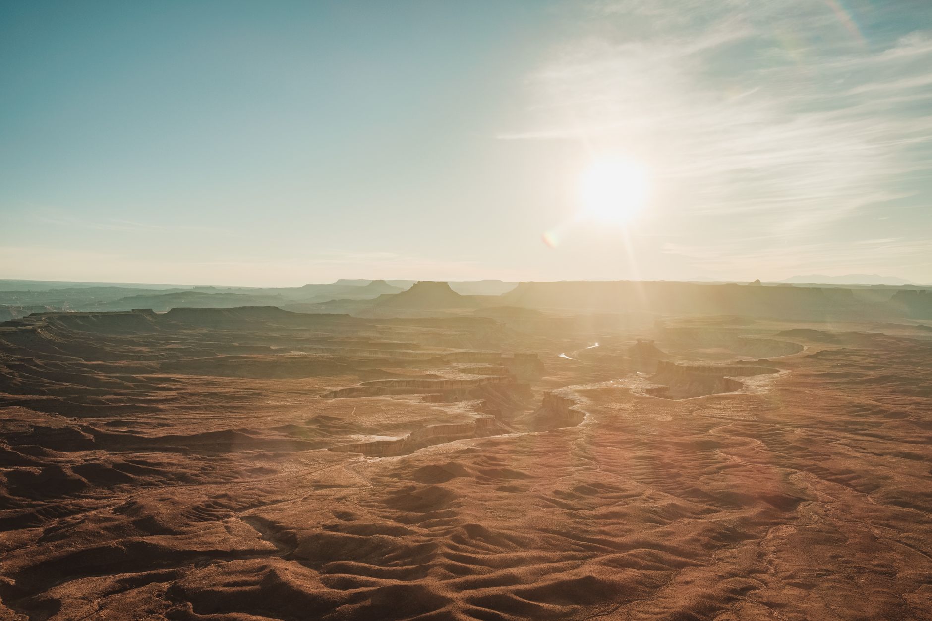 An empty two-lane highway stretches through a vast, dramatic desert landscape under a wide-open sky, suggesting a long road trip into remote territory.