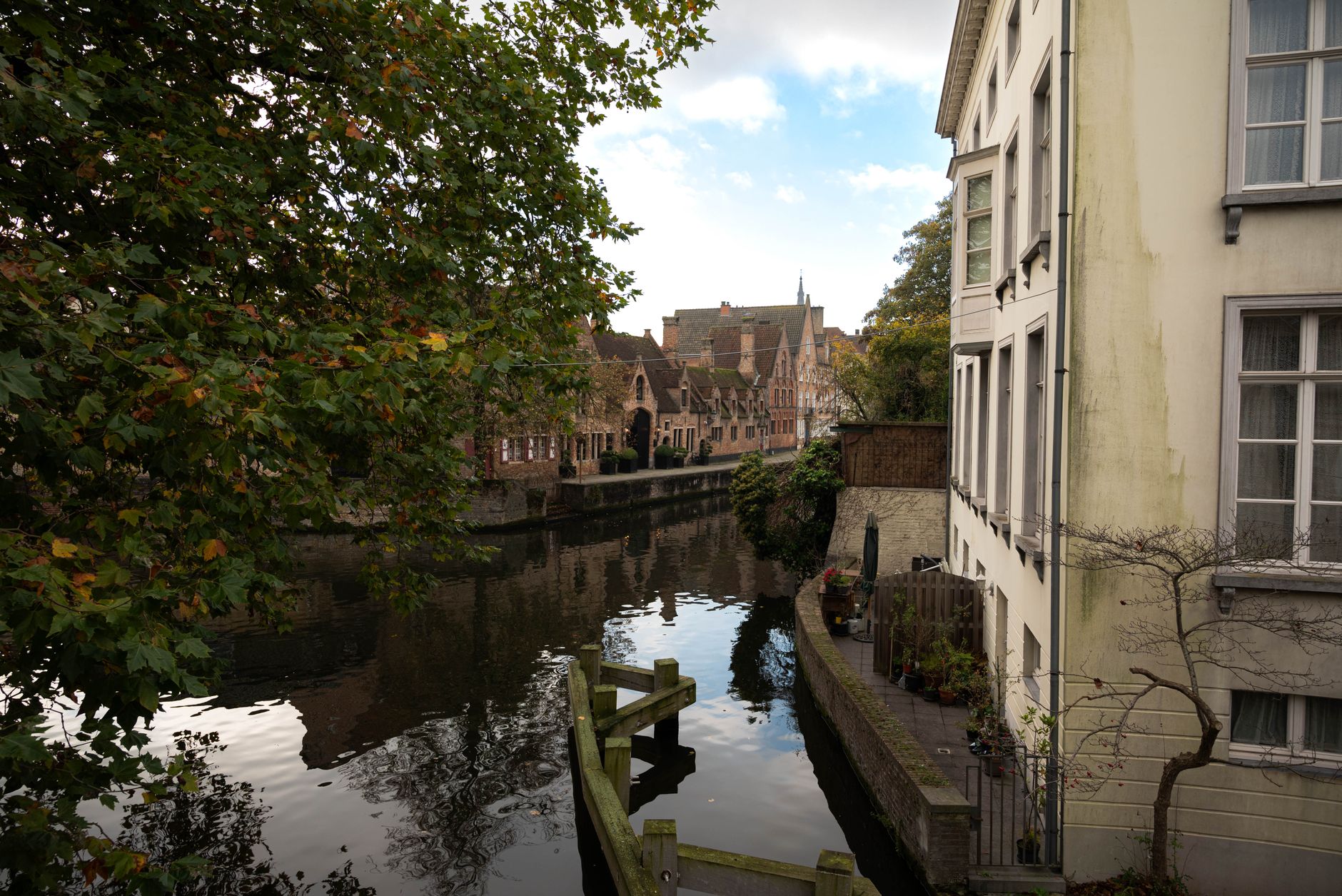 A quiet, narrow canal in Bruges winding past medieval brick buildings under a soft evening sky, with no visible tourists.