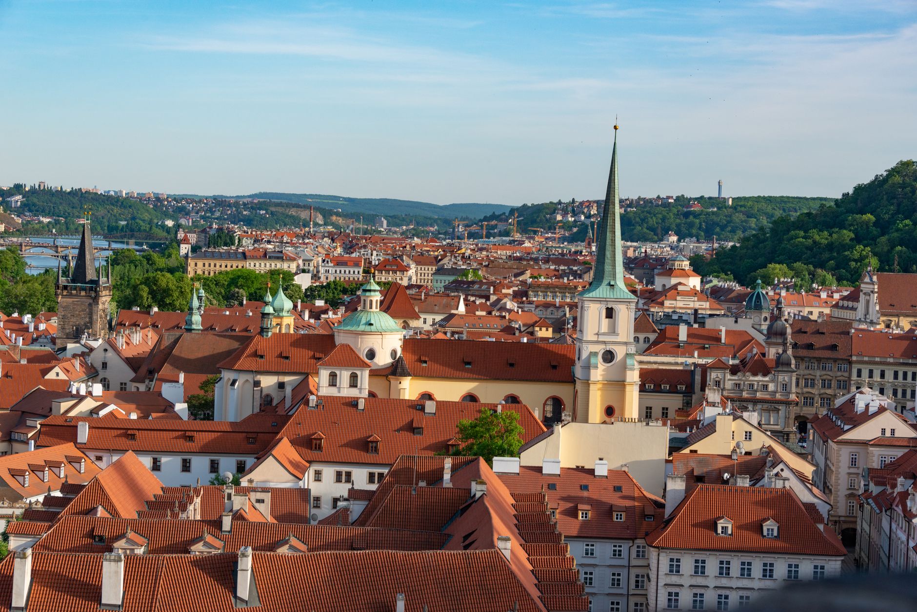 Sweeping panoramic view of Prague's historic skyline, featuring red rooftops and prominent landmarks at sunset.