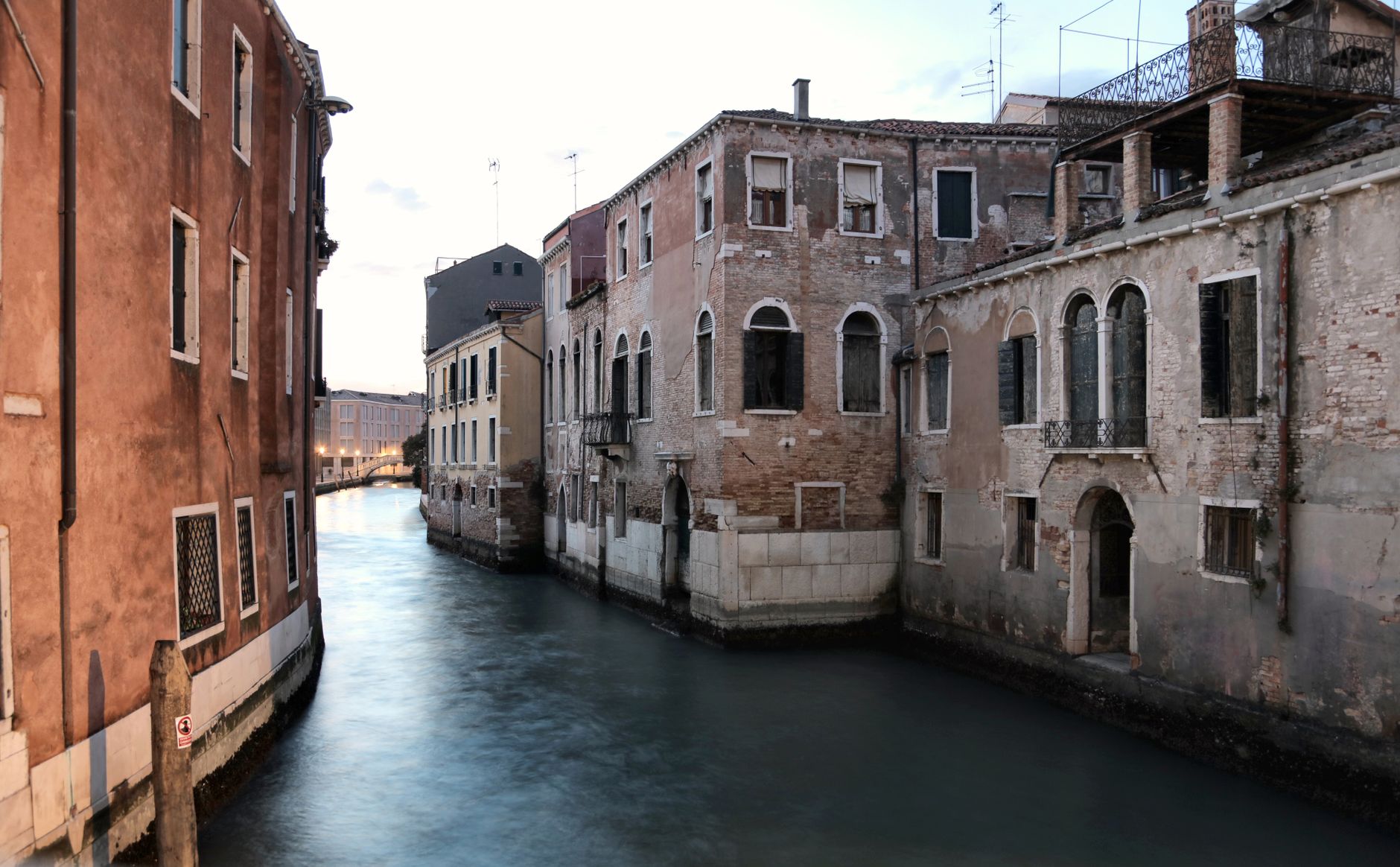 A tranquil, less-traveled canal in Venice at dawn, showing quiet historic buildings and a lone gondola, hinting at the city's hidden beauty.