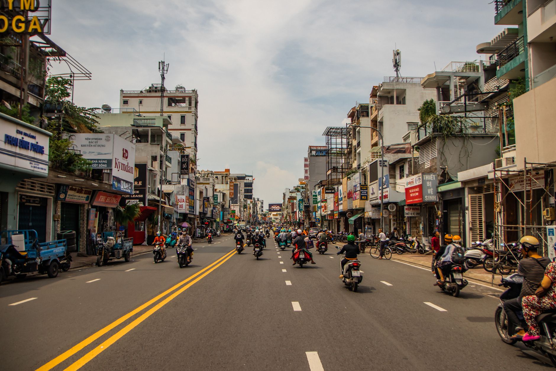 A bustling street scene in Thảo Điền, Ho Chi Minh City, with motorbikes, street vendors, and lush greenery, hinting at hidden culinary delights.
