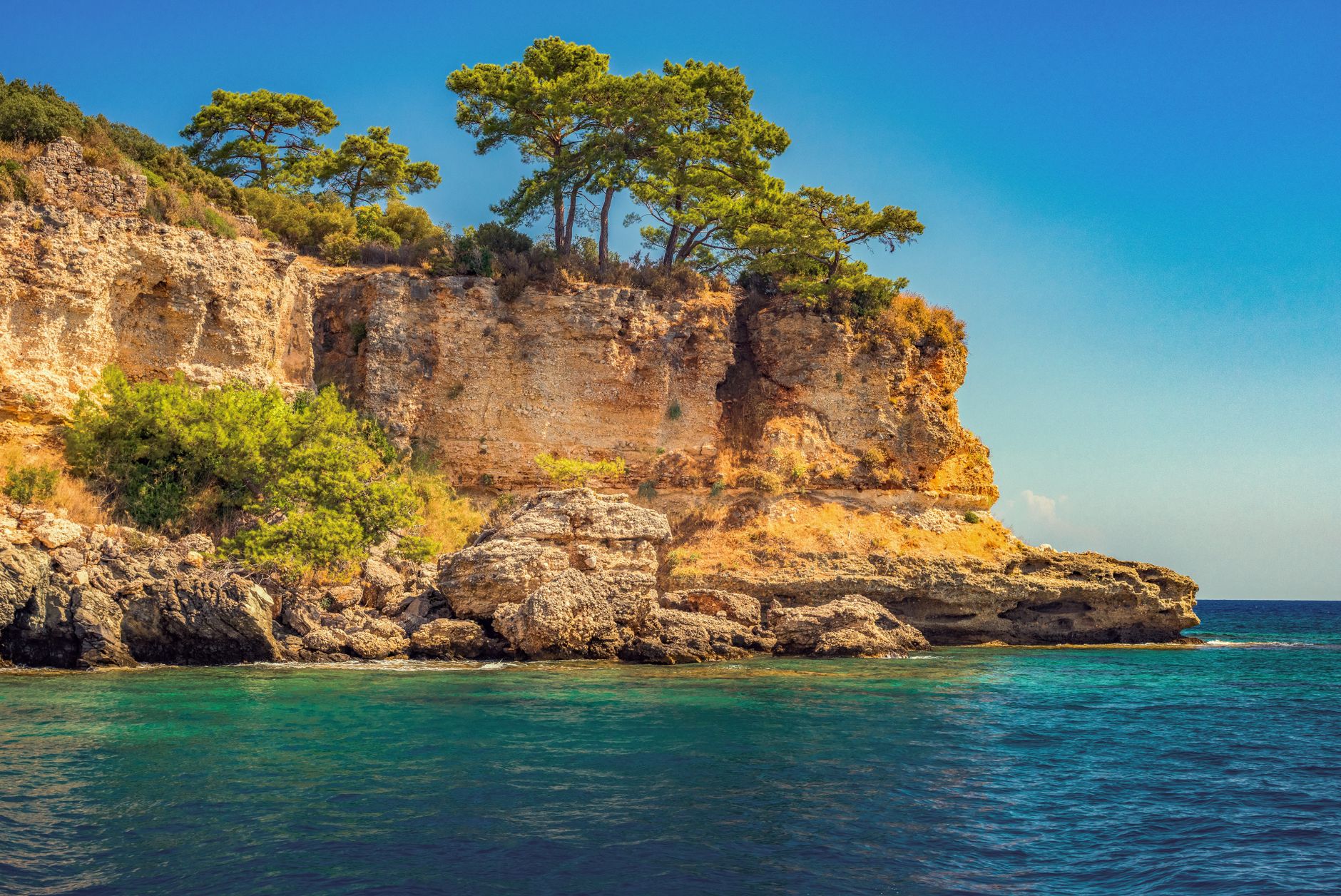 Sweeping view of a pristine, uncrowded European beach with clear turquoise waters and rugged coastline under a bright sun