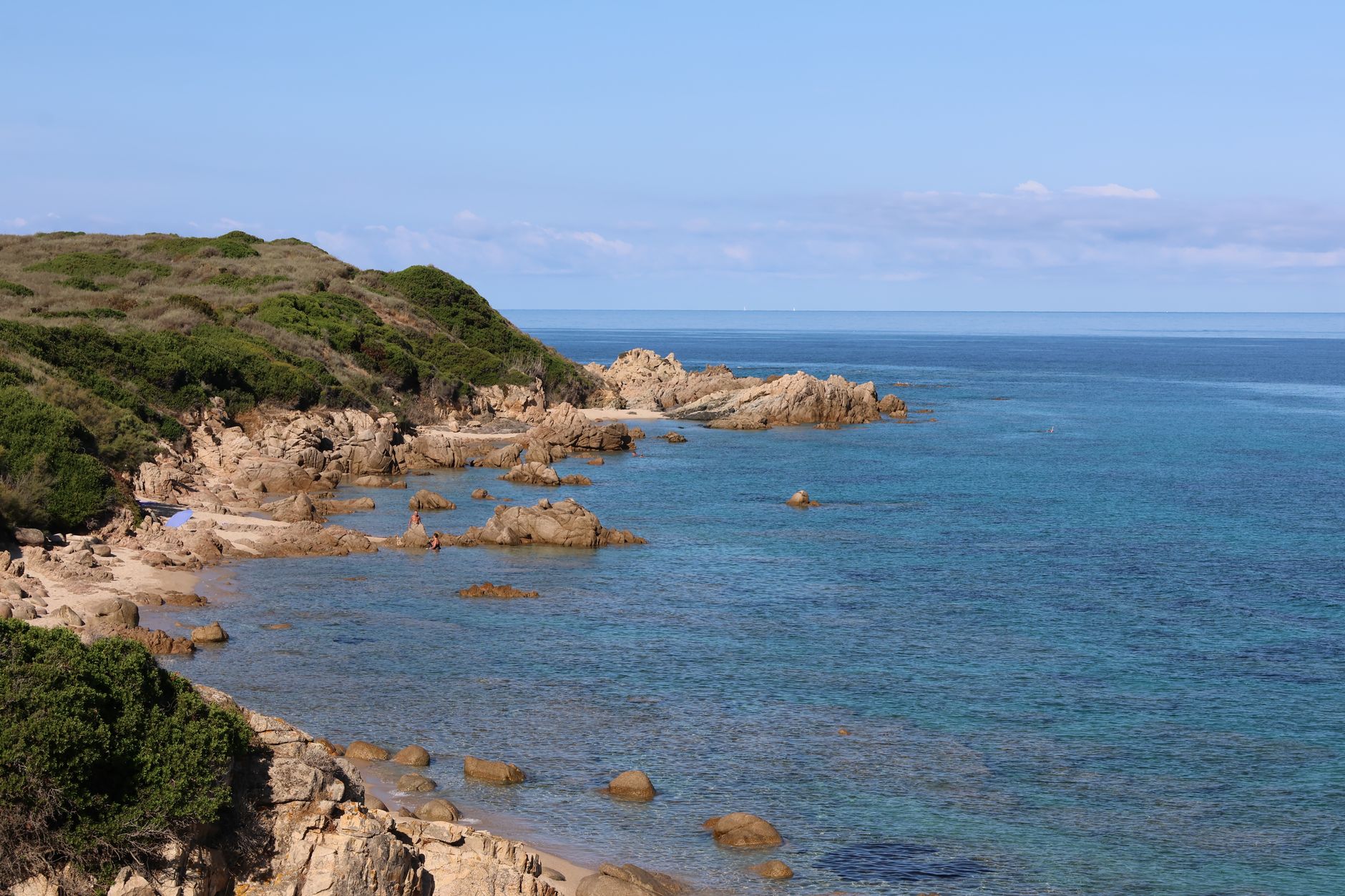 A sweeping panoramic view of a dramatic, secluded Italian coastline with clear turquoise waters, jagged cliffs, and untouched sandy coves under a bright sky.