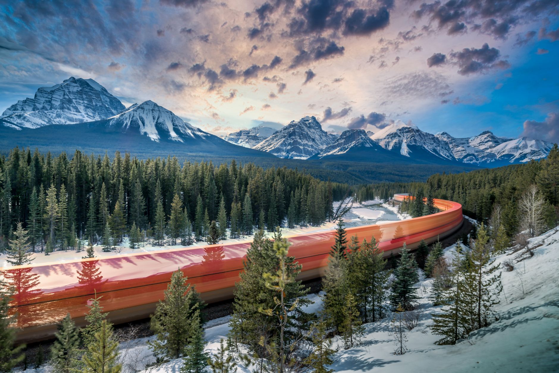 A vintage train, possibly a VIA Rail classic, cutting through a vibrant Canadian autumn landscape between two major cities.