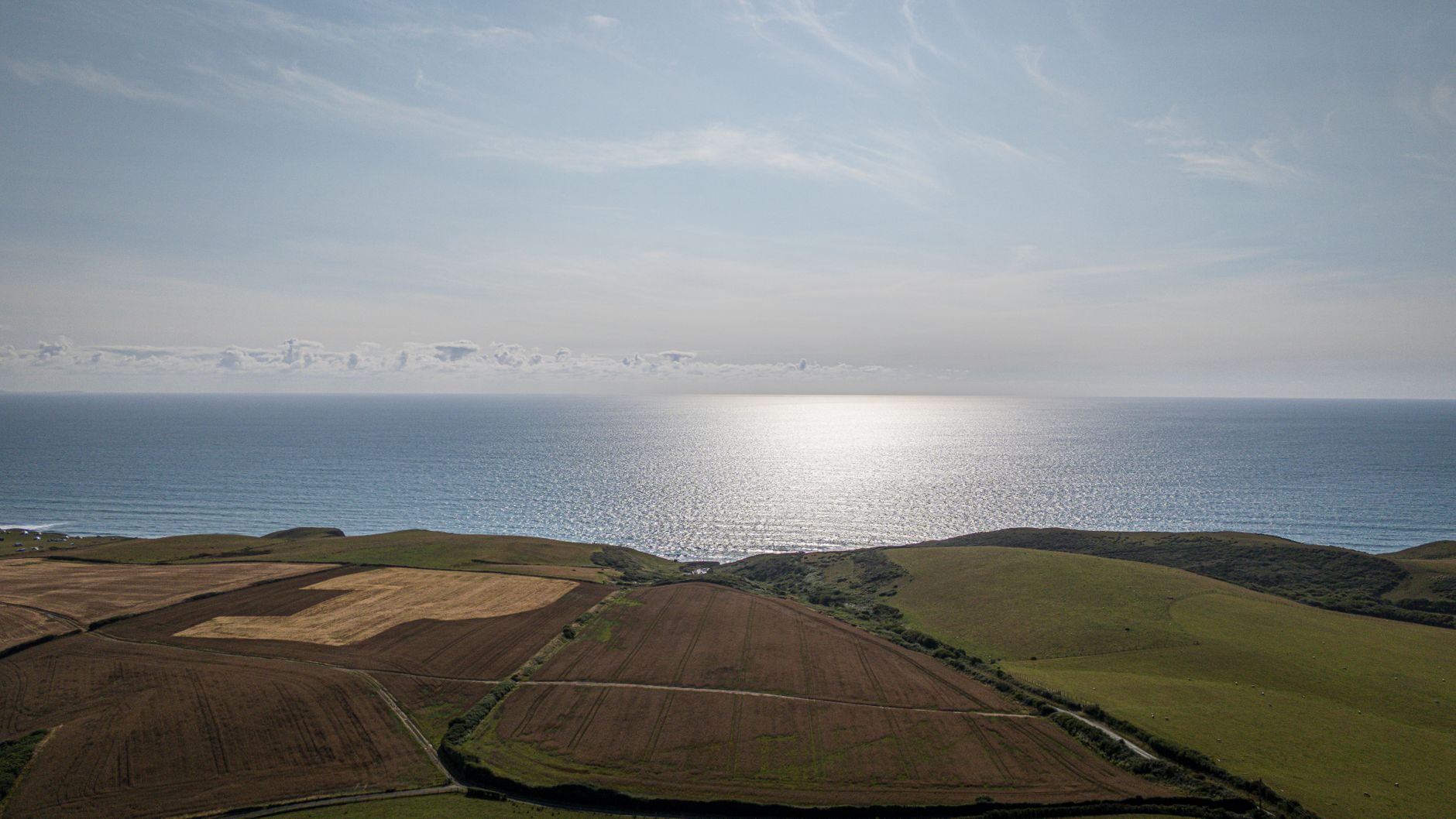 A sweeping view of a sunlit British coastline with chalk cliffs meeting a calm, blue sea under a clear sky.