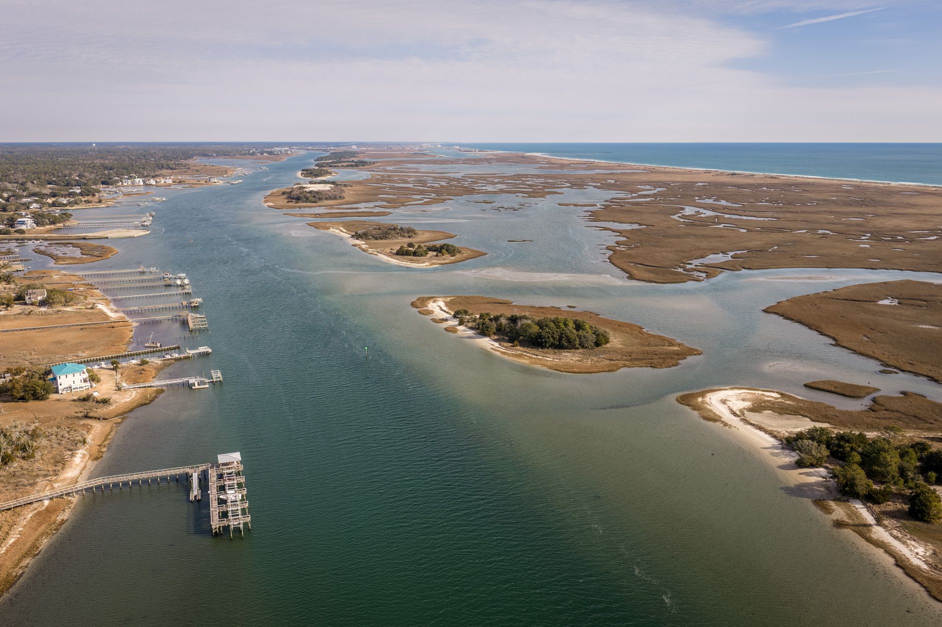 Sweeping aerial view of a pristine South Carolina barrier island coastline at sunset, with vast salt marshes stretching inland.