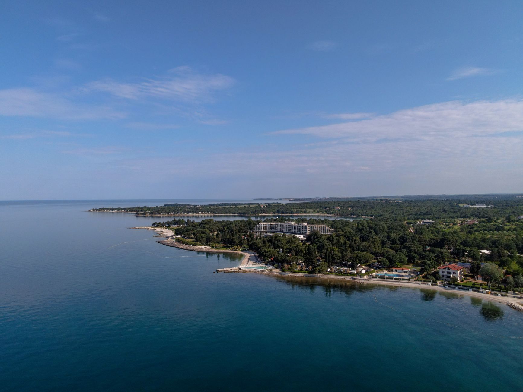Sweeping aerial view of Croatia's rugged coastline meeting the azure Adriatic Sea, with a small, ancient village perched on a cliff edge under a clear sky.