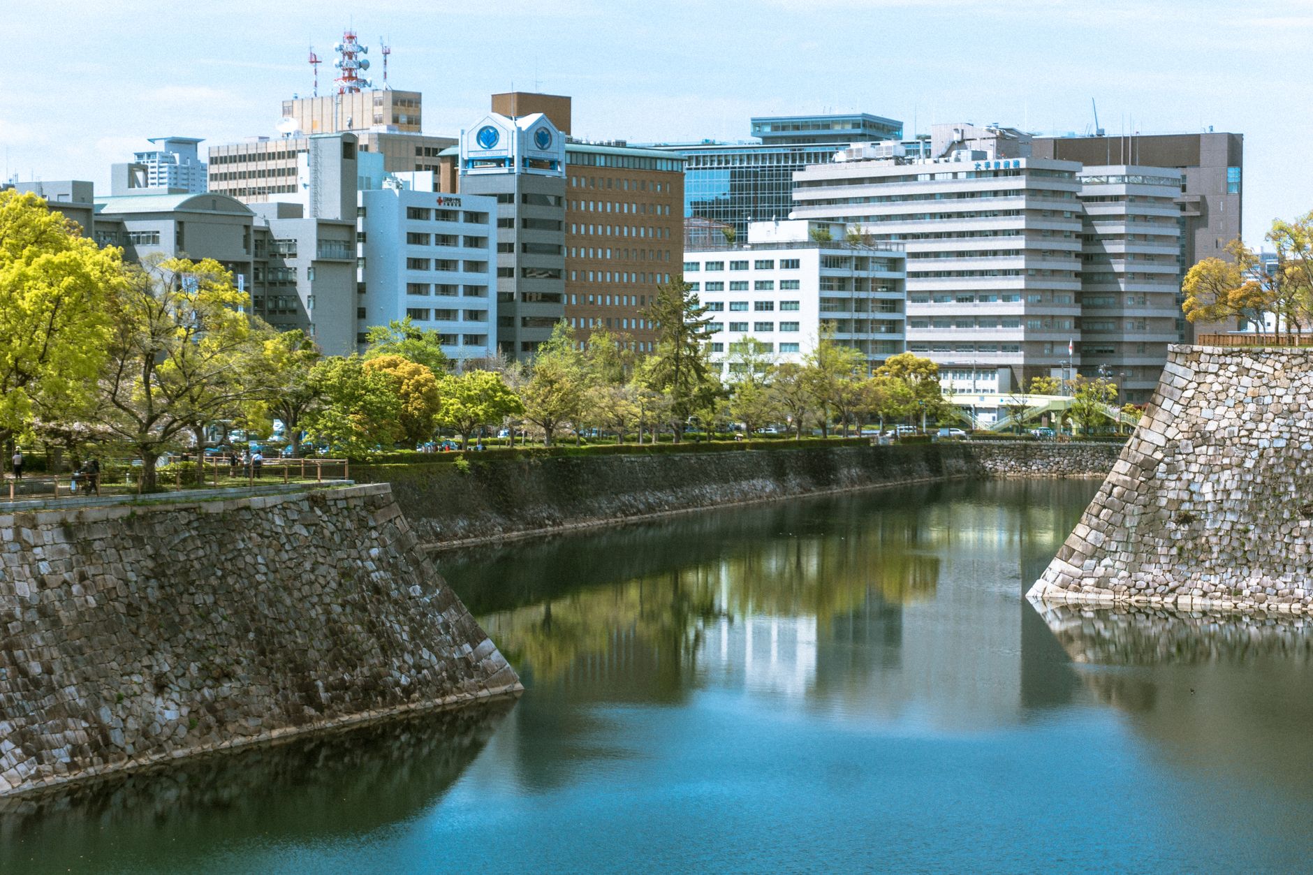 A panoramic view of Hiroshima city at dusk, showing a mix of modern buildings and green spaces, with a mountain range in the background.