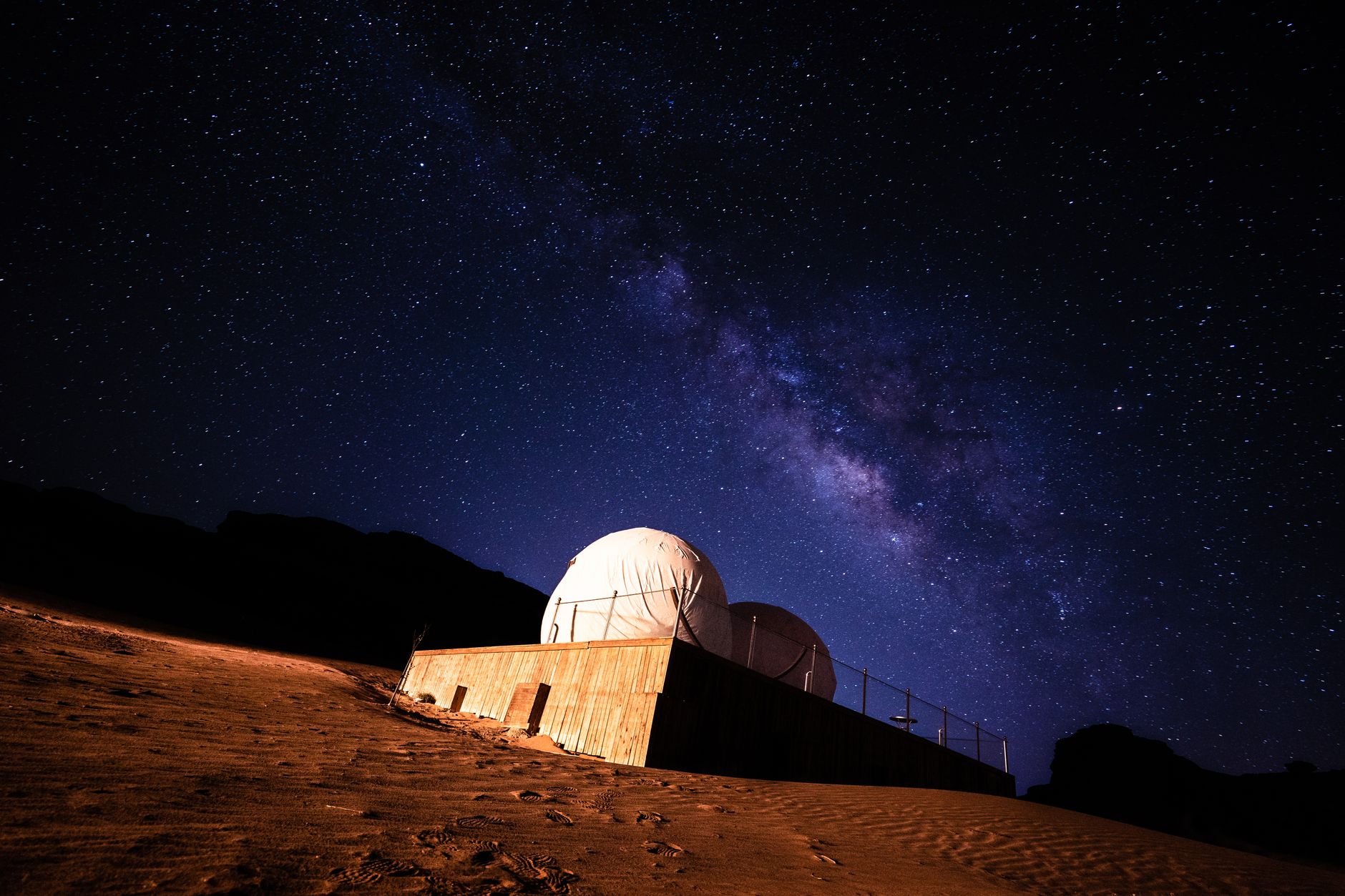 A panoramic view of a vast, star-filled desert landscape with distant rock formations under a twilight sky, evoking mystery and adventure.