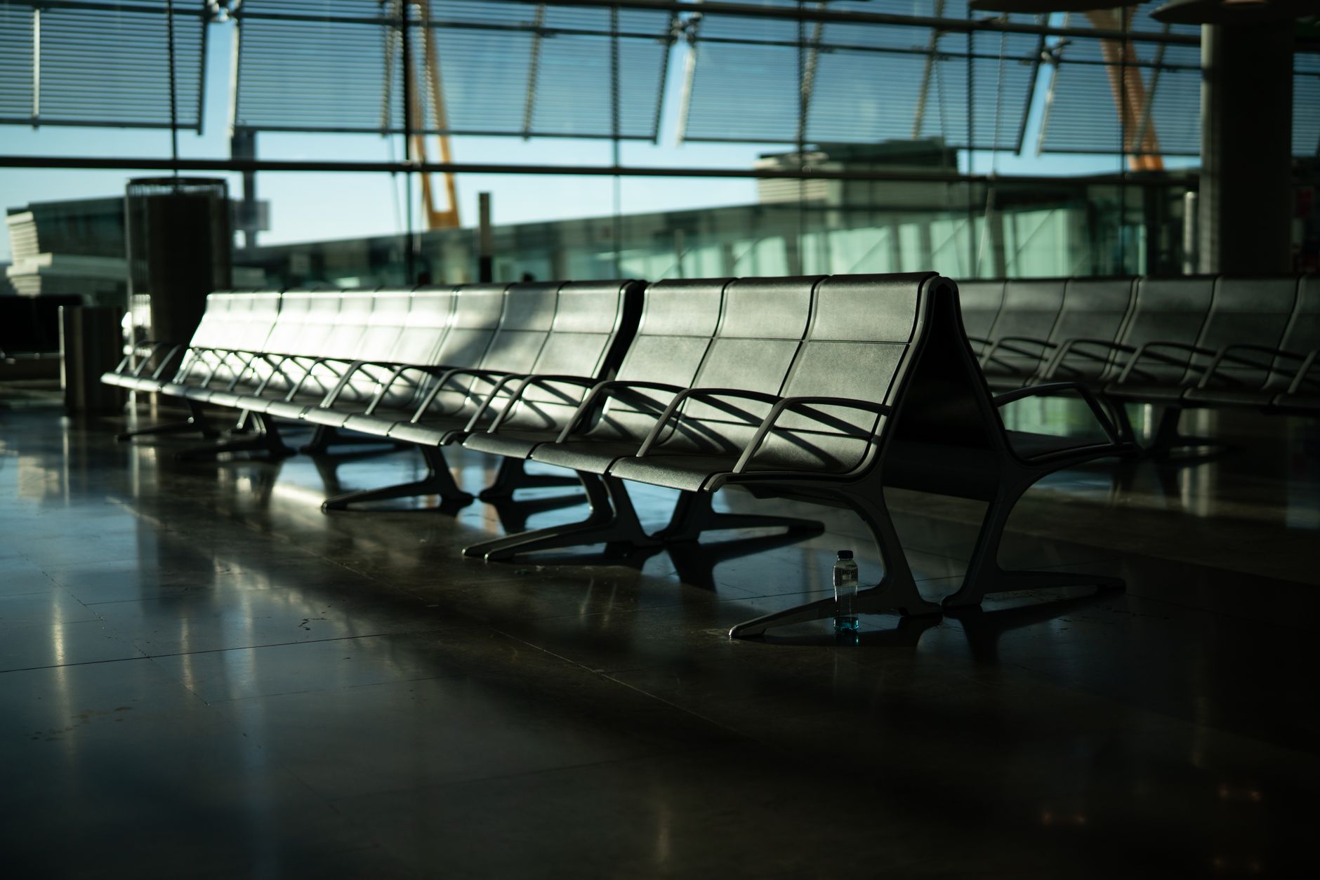 A traveler looking thoughtfully out an airport terminal window at a distant, hazy mountain range, symbolizing the vast world of hidden wonders beyond the airport.