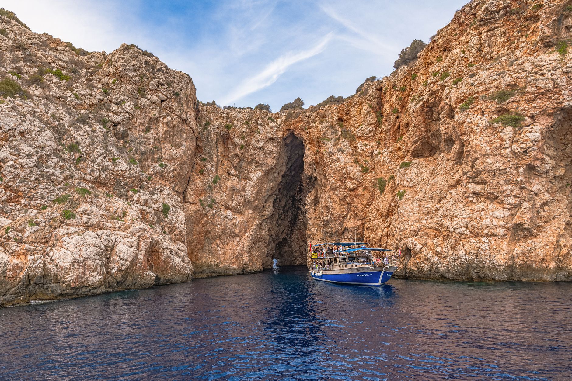 A small traditional boat navigating serene, clear waters surrounded by dramatic, lush green mountains under a bright sky, suggesting a remote and beautiful journey.