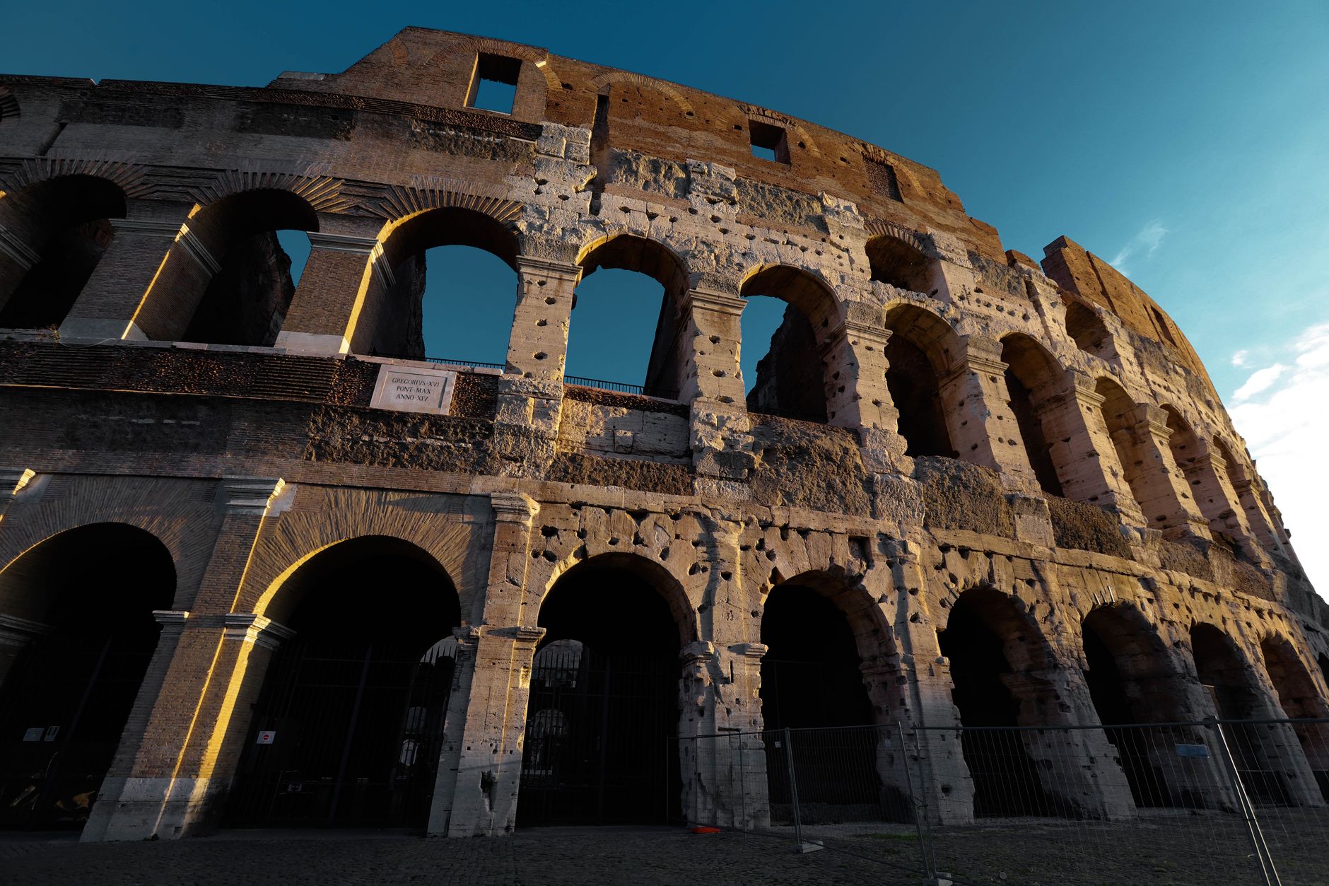 A wide, sweeping view of ancient, weathered stone ruins under a dramatic sunset sky, evoking a sense of forgotten history and mystery.