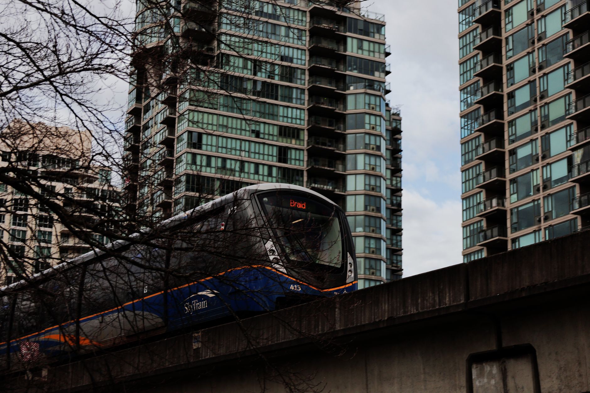 A Skytrain train moving through a modern Vancouver cityscape with mountains in the background, showcasing the city's public transport.