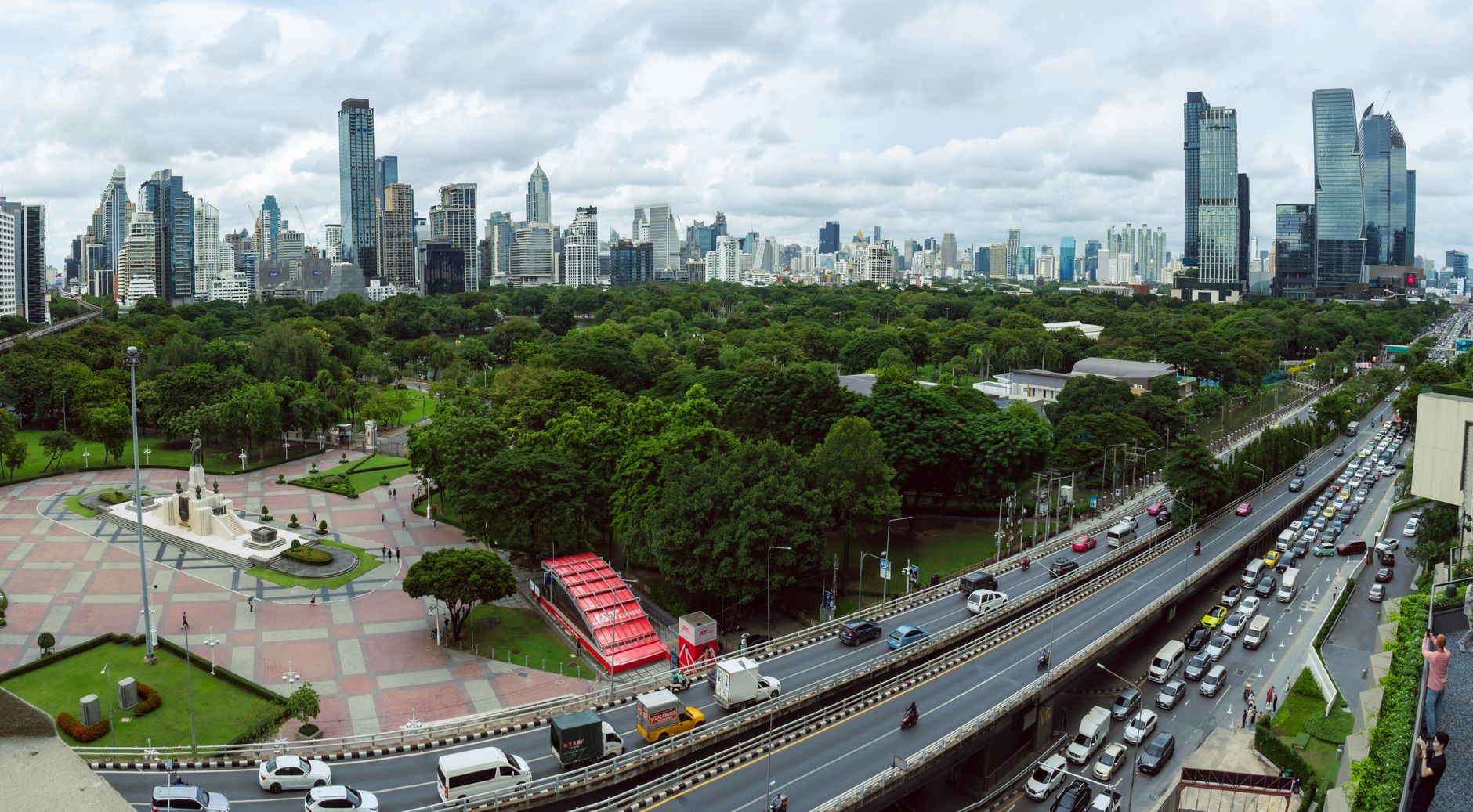Sweeping aerial view of a lush green artificial island, Bang Krachao, nestled within a bend of the Chao Phraya River, contrasting with distant Bangkok skyscrapers.