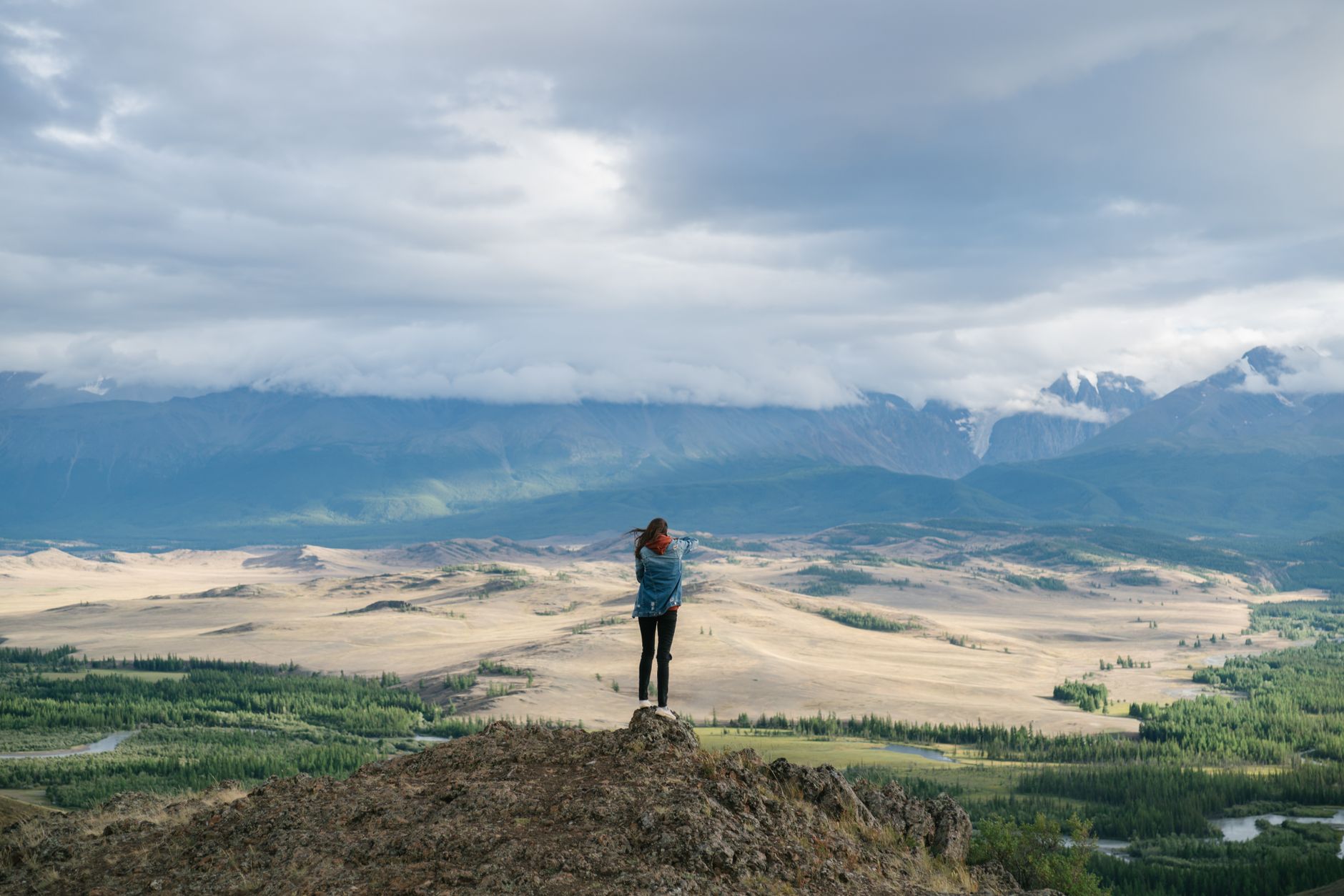 A lone traveler stands on a vast, otherworldly landscape, camera in hand, looking out at a stunning geological formation under a dramatic sky.